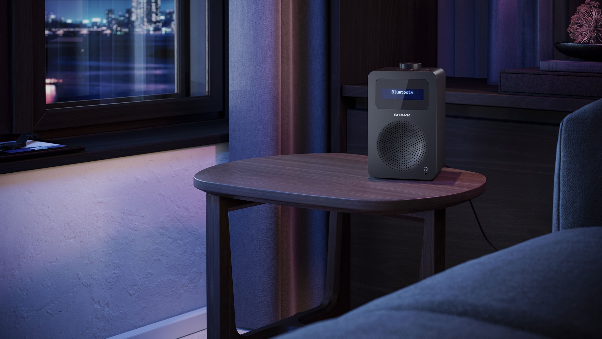 Czarny radioodtwarzacz Sharp z wyświetlaczem „Bluetooth” stoi na drewnianym stole. Okno pokazuje światła miasta. Widoczna jest sofa i zasłona.