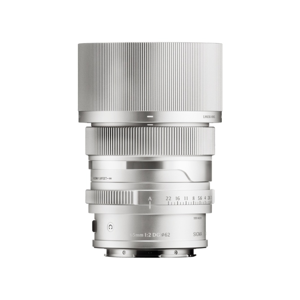 Un objetivo Sigma 65mm f/2 DG plateado se alza sobre un fondo blanco. Tiene secciones acanaladas y marcas de medición.