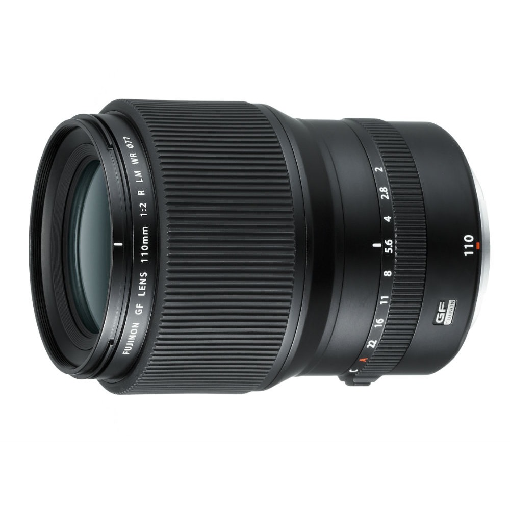 Een zwarte Fujinon GF lens, model 110mm 1:2 R LM WR 077, ligt op een wit oppervlak. Het heeft focus- en diafragmaringen.