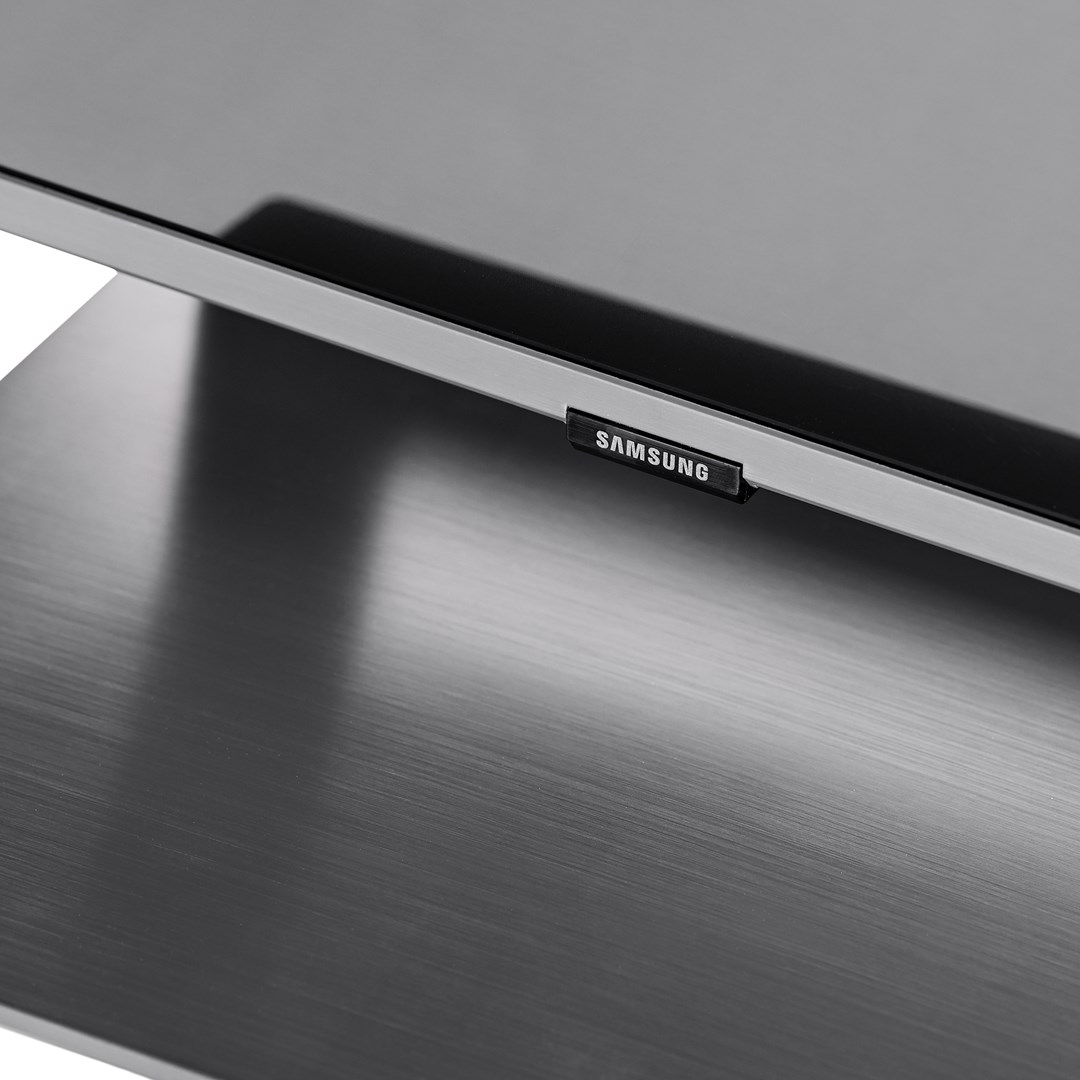 Close-up of a Samsung TV. The screen is black. The stand is metallic, with the Samsung logo visible.