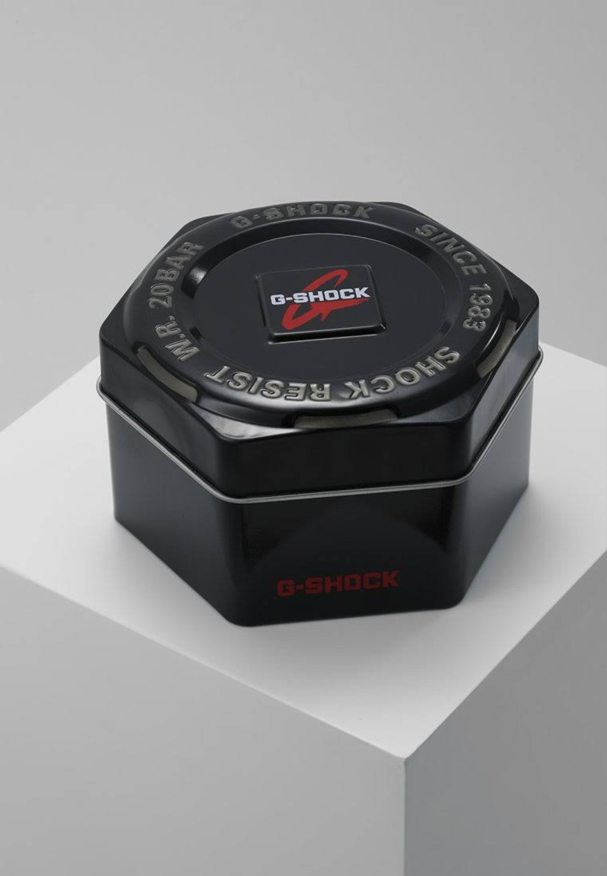 Caja negra de reloj G-Shock sobre una superficie blanca. La caja es hexagonal con el logo y texto rojo de G-Shock.