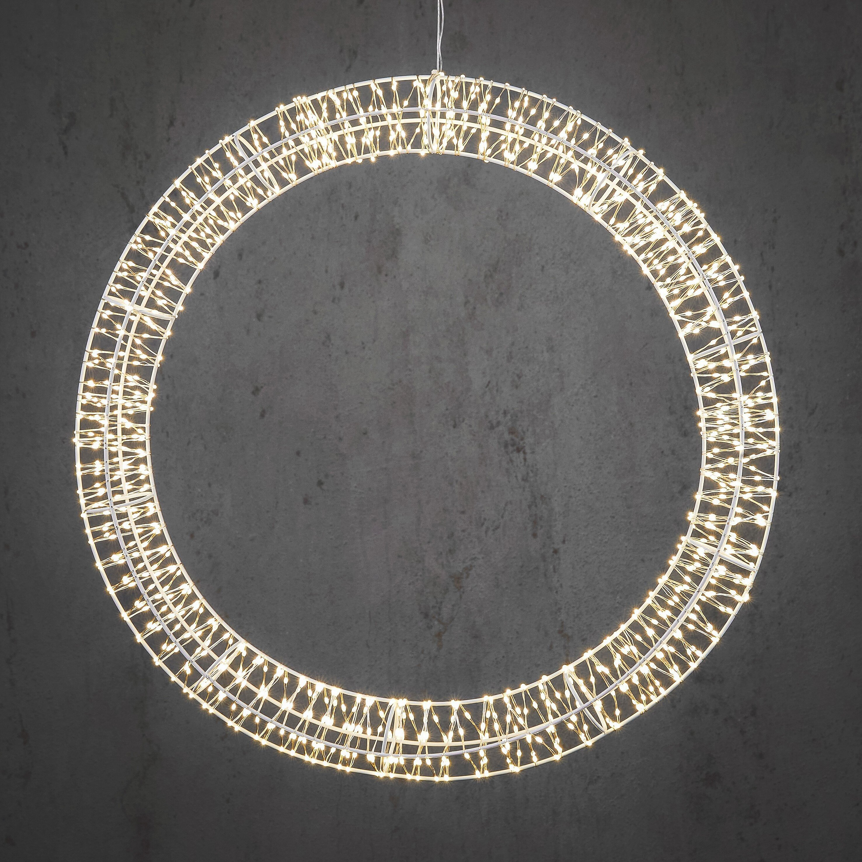 Un luminaire circulaire avec de petites lumières blanc chaud est suspendu sur un fond de béton gris.
