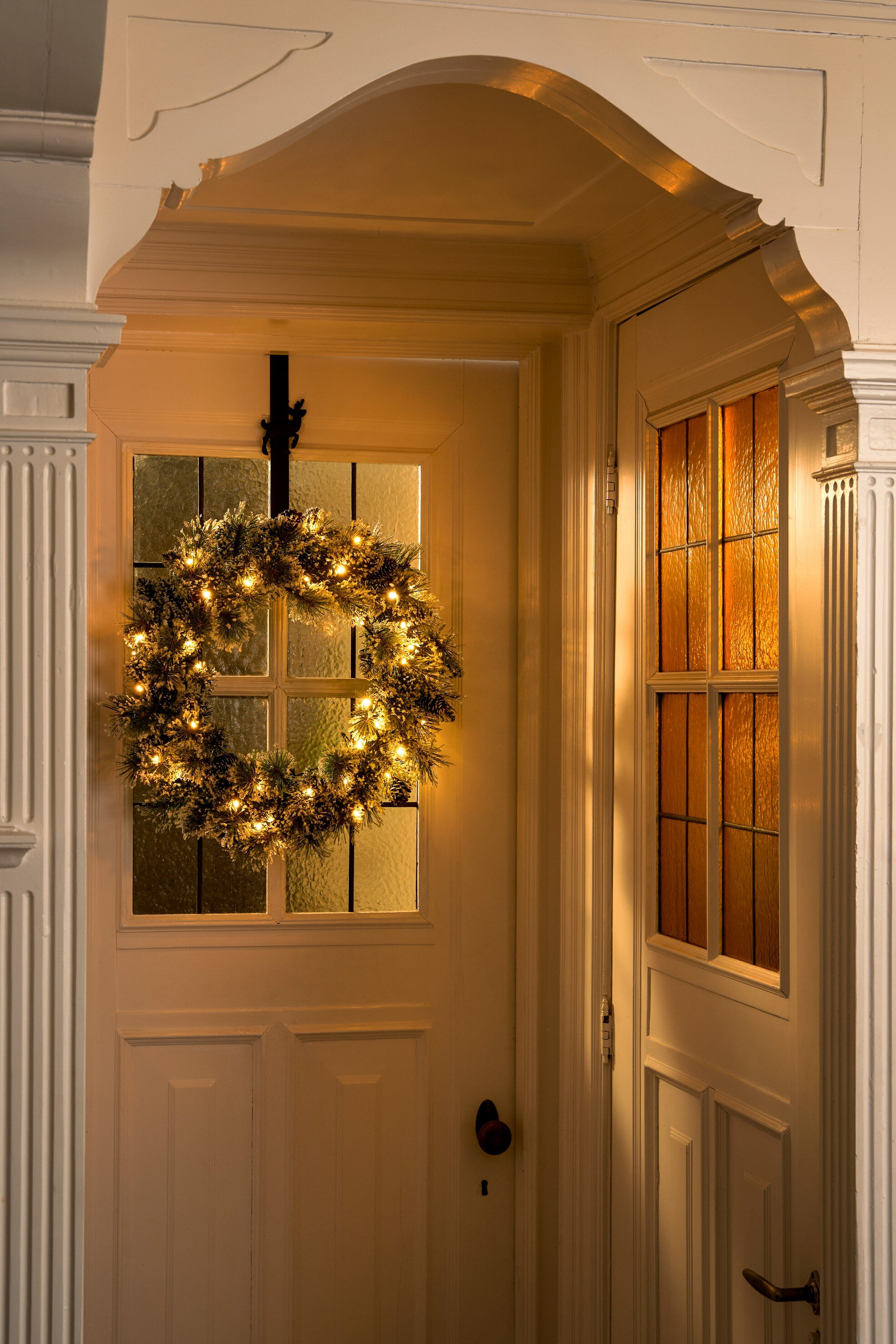 Une porte blanche avec une couronne lumineuse et une porte avec un panneau de verre orange. Décorations de Noël.