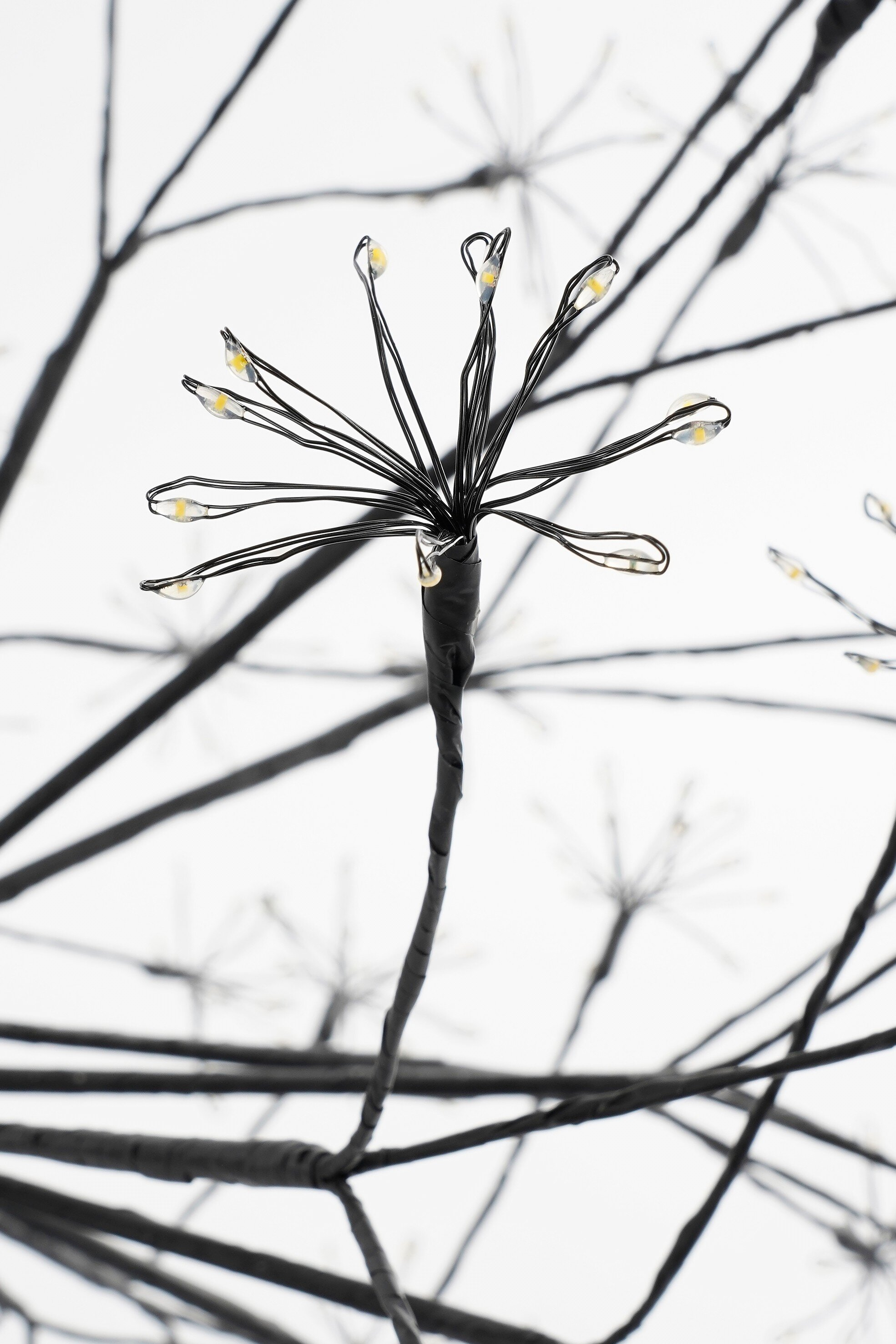 Gros plan d'un luminaire décoratif avec des branches noires et de petites lumières LED vives sur fond blanc.