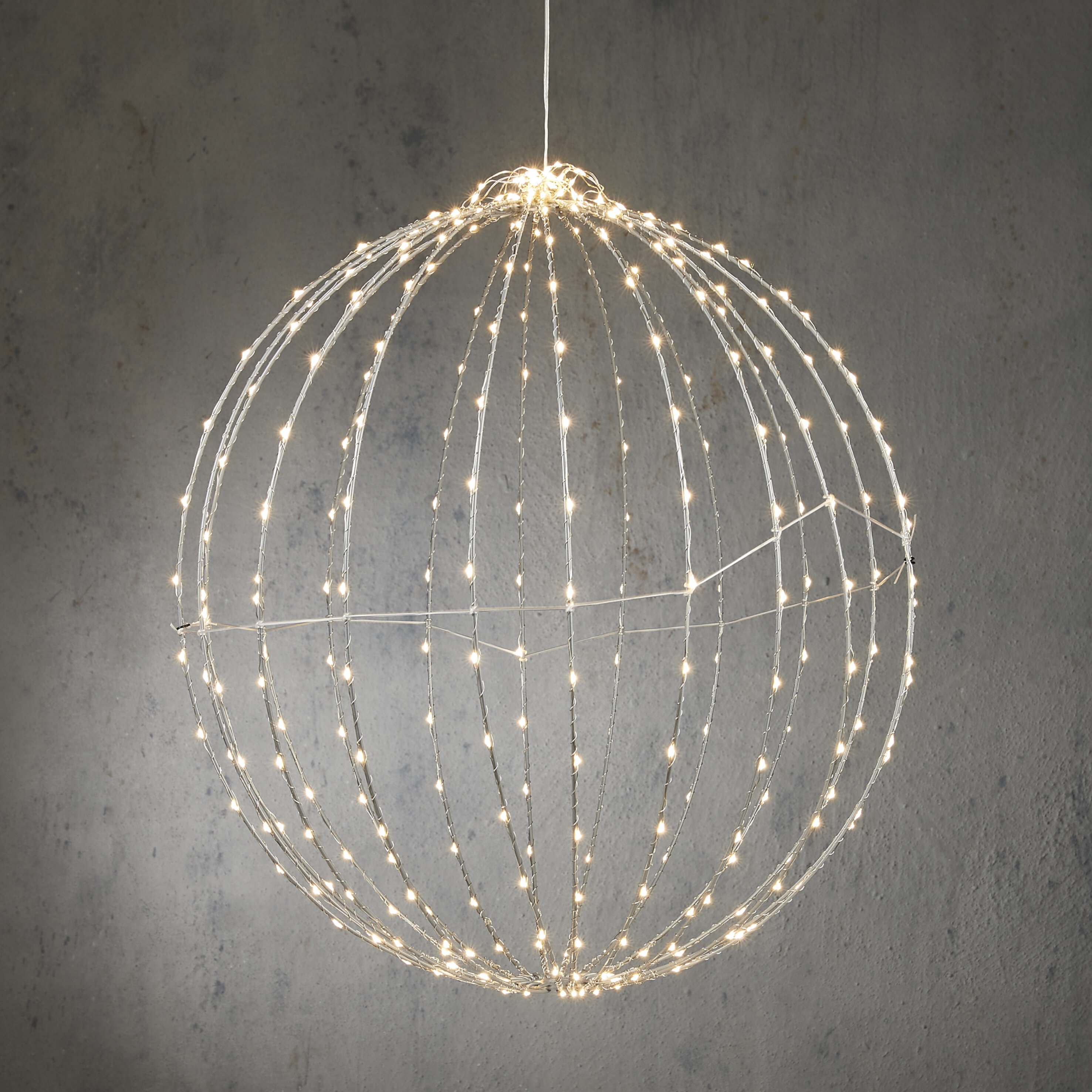 Une sphère décorative avec de nombreuses petites lumières est suspendue contre un mur gris. La sphère est en fils de métal.