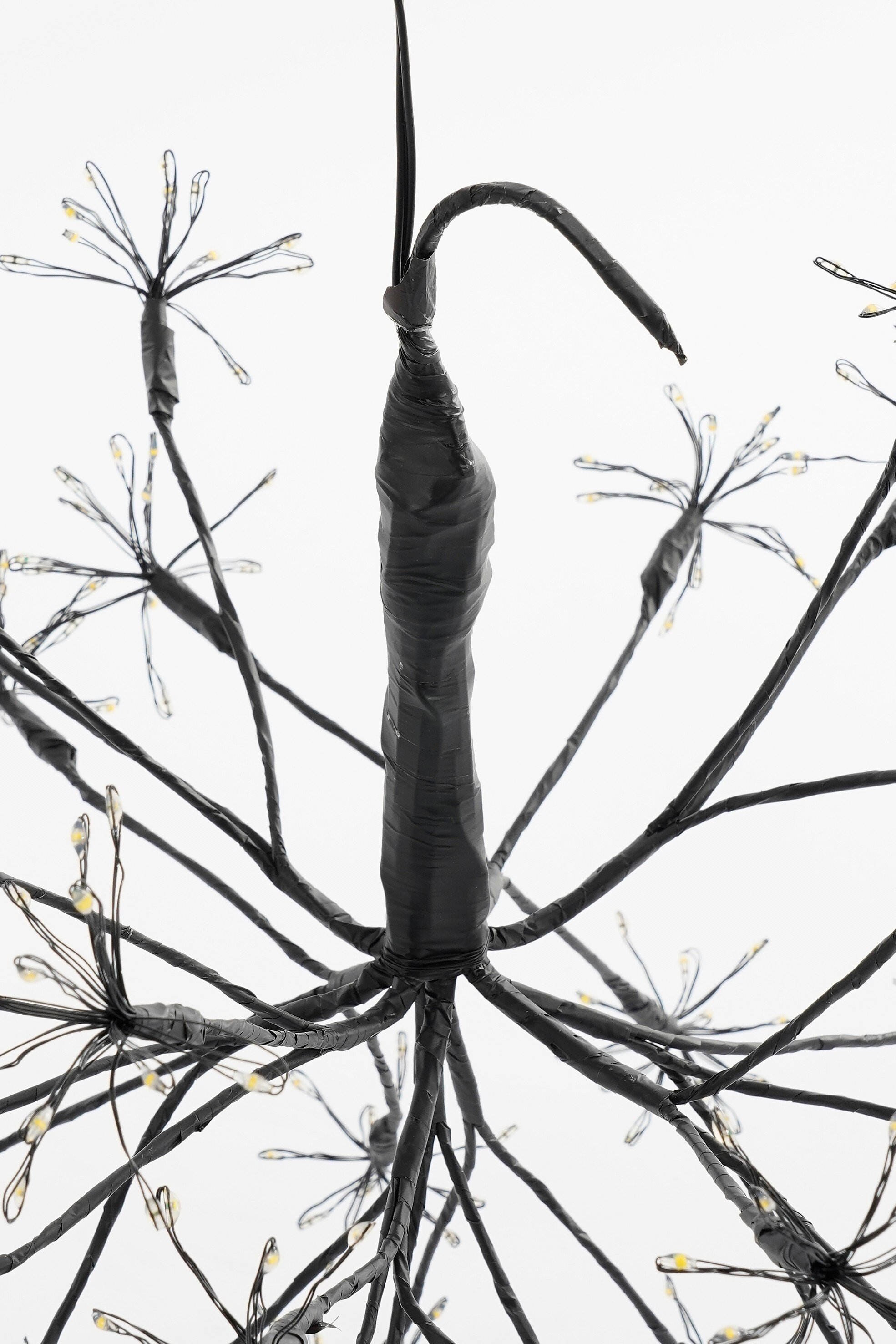 Gros plan d'une décoration noire en forme d'arbre avec de petites lumières jaunes sur fond blanc.
