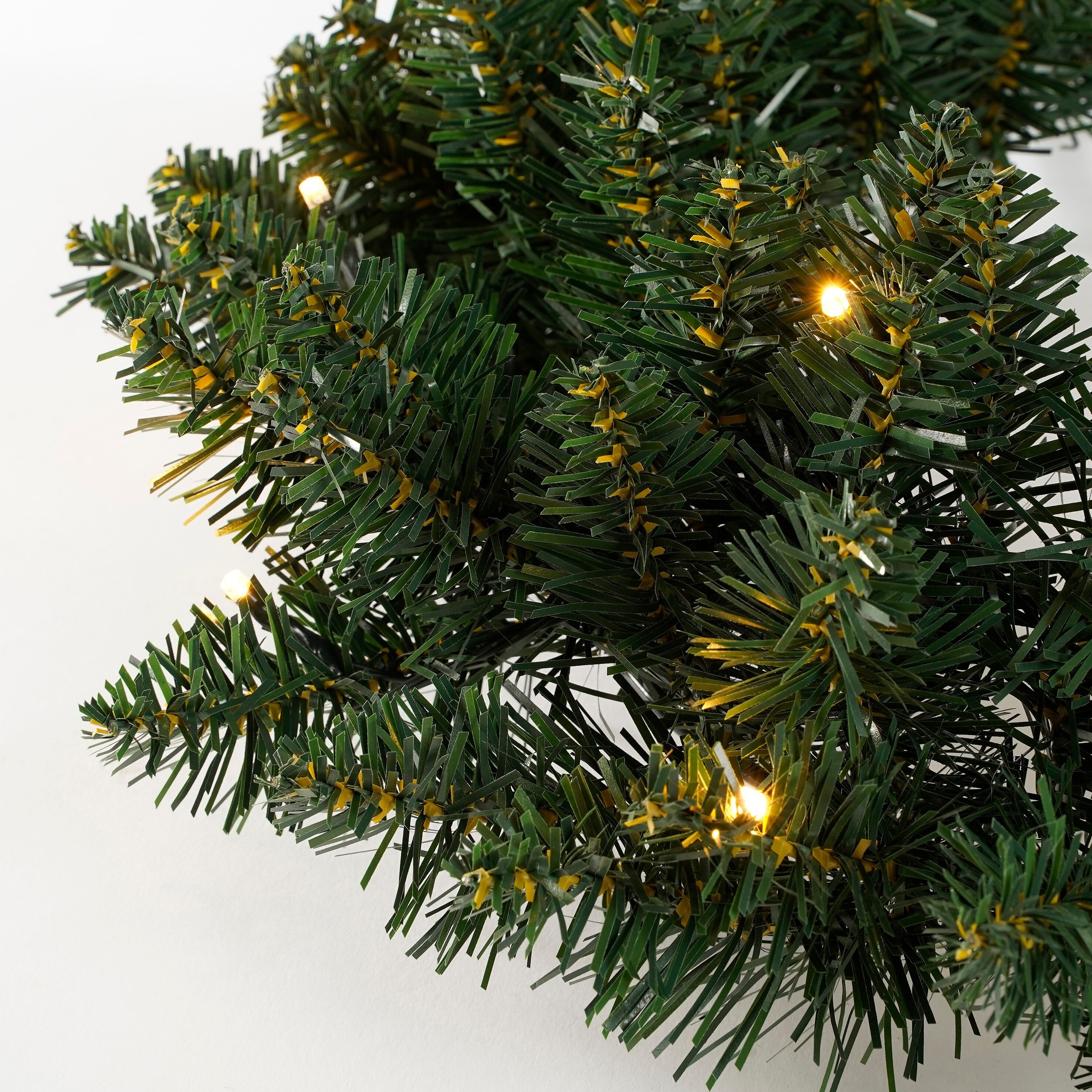 Gros plan de branches de sapin de Noël artificielles avec des accents jaunes et de petites lumières brillantes sur fond blanc.