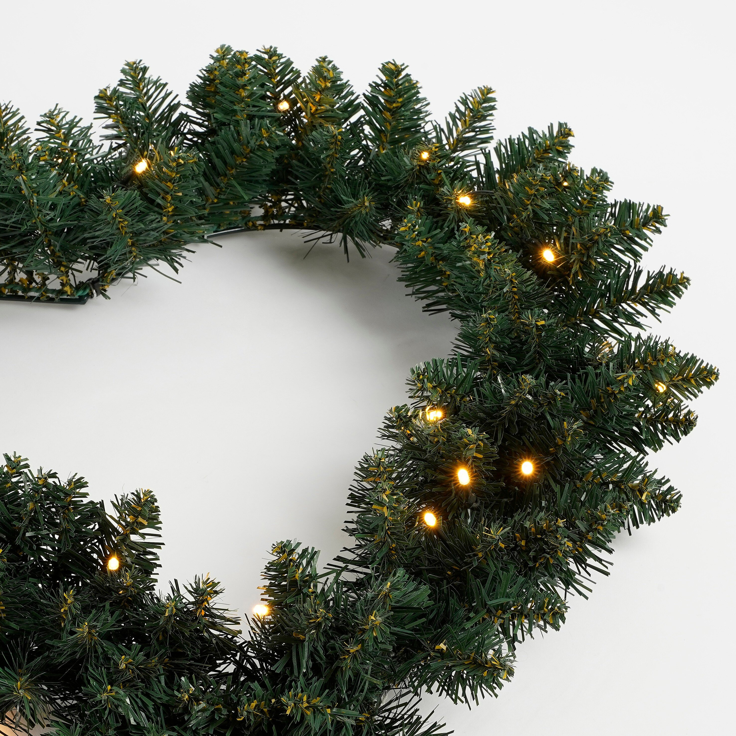 Une couronne de Noël verte avec des lumières jaunes sur fond blanc. La couronne est circulaire.