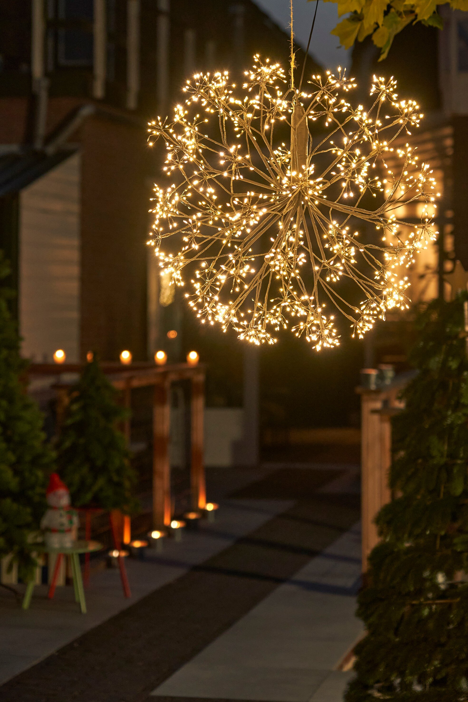 Un luminaire en forme d'étoile brillante est suspendu à l'extérieur. Des arbres verts et une figurine de bonhomme de neige sont visibles.