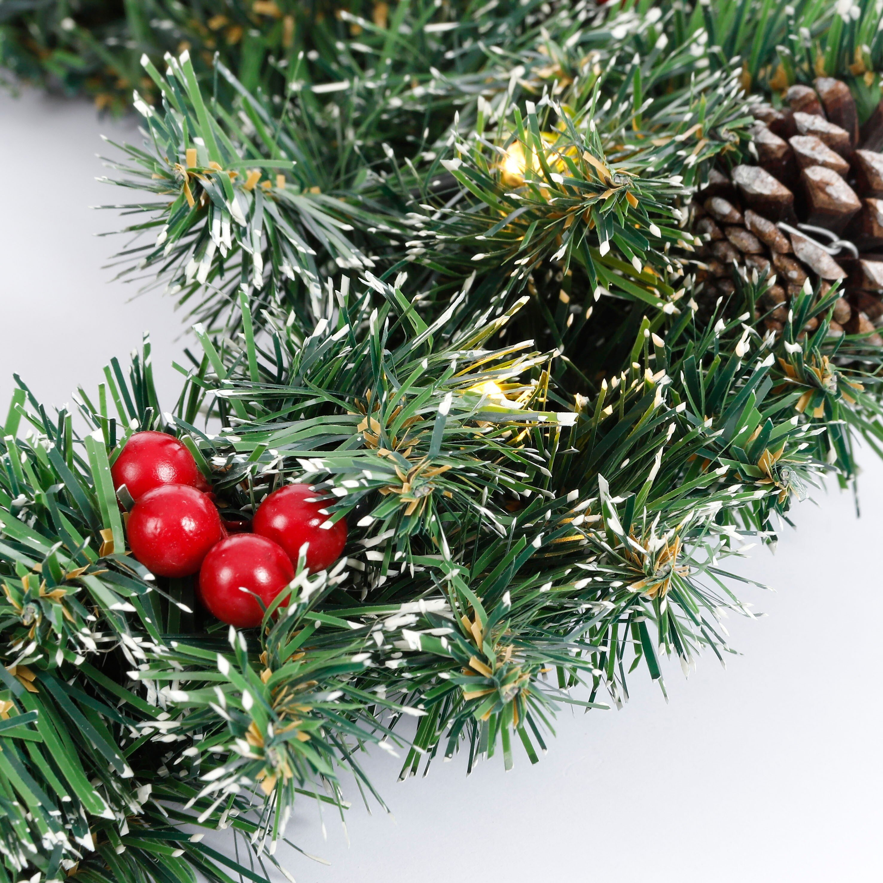 Gros plan d'une couronne de Noël avec des aiguilles de pin, des baies rouges, une pomme de pin et de petites lumières.