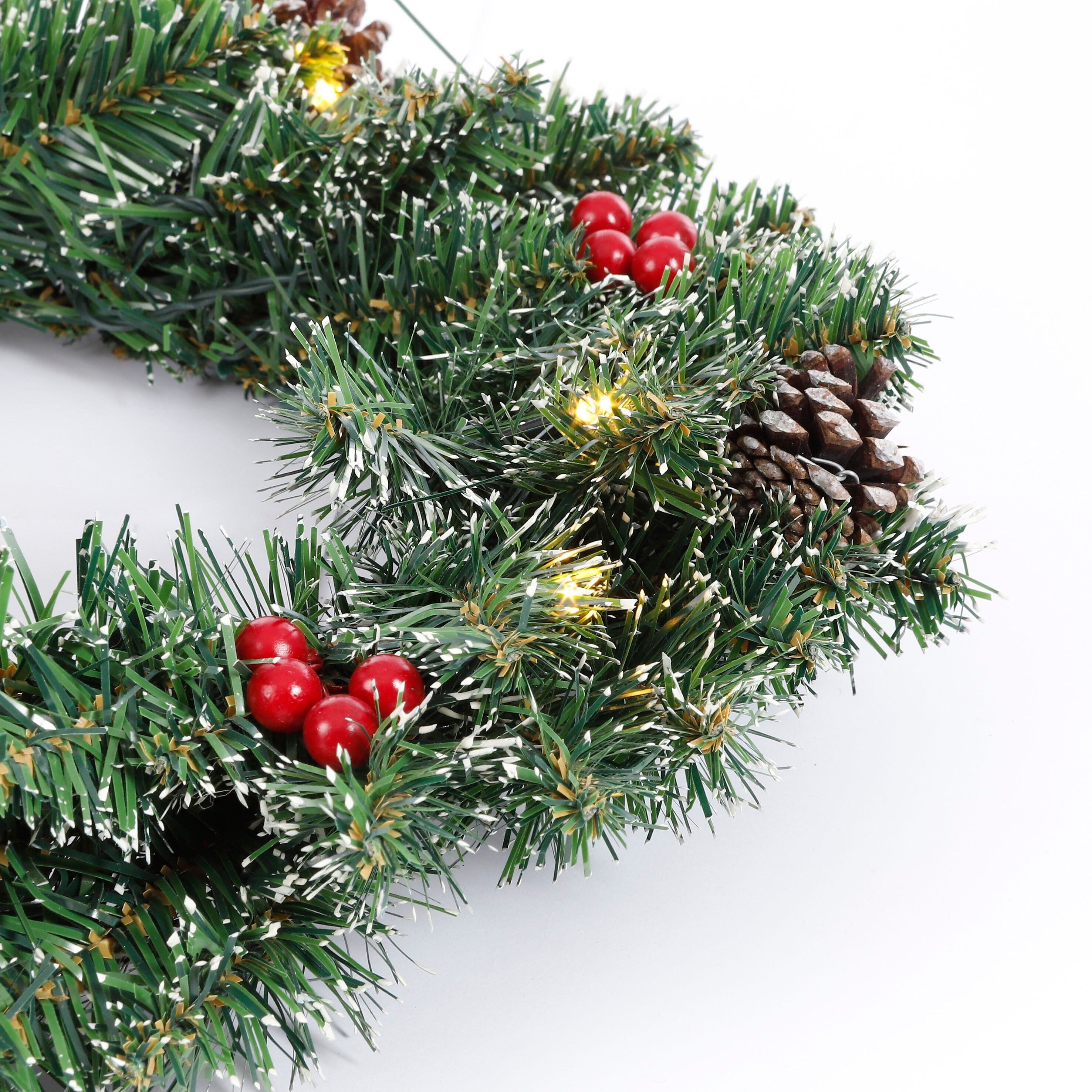 Gros plan d'une guirlande de Noël. Aiguilles vertes, baies rouges, une pomme de pin et des accents blancs sont visibles.