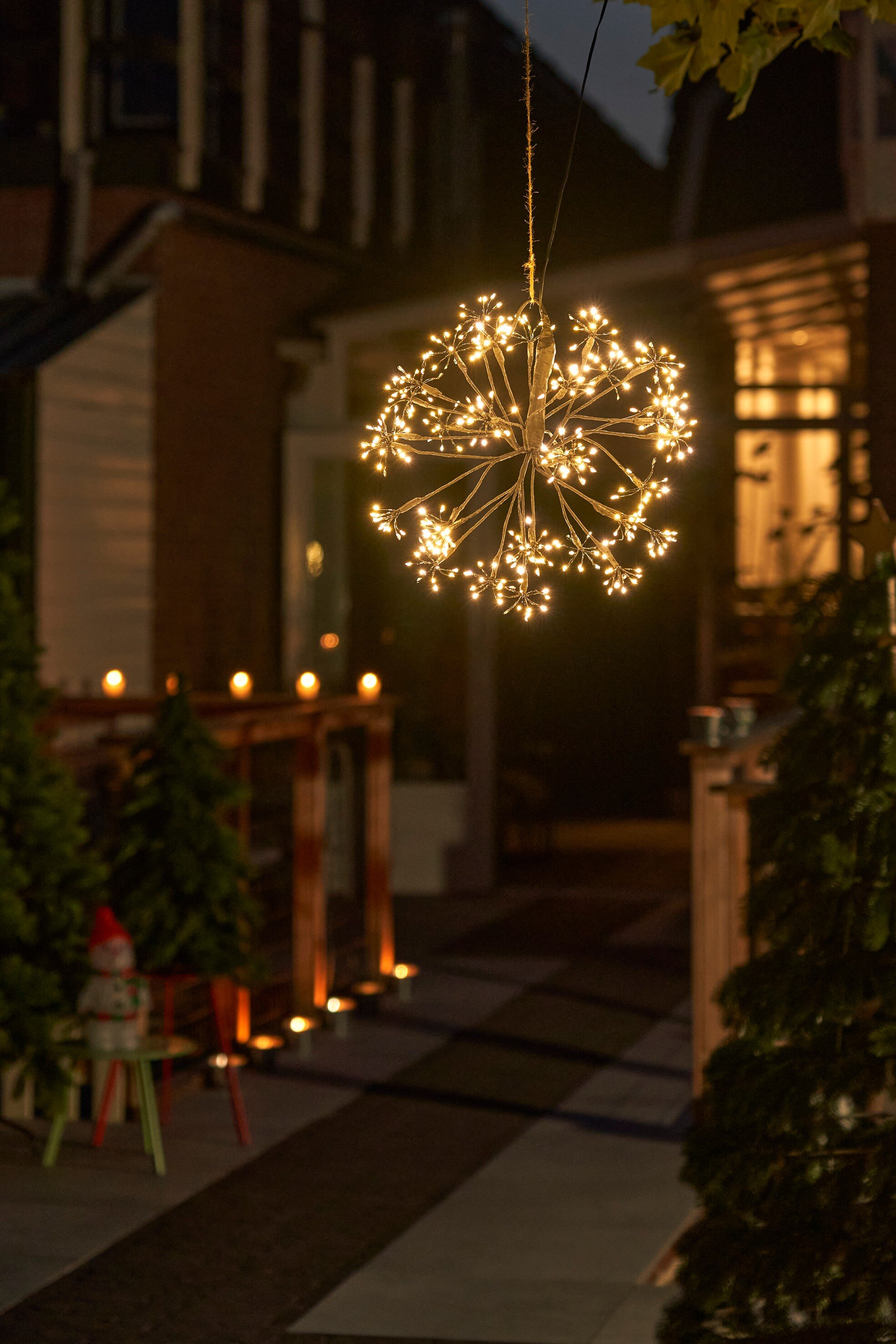 Une lumière éclatante en forme d'étoile est suspendue à l'extérieur d'une maison la nuit. De petits sapins et lumières en arrière-plan.