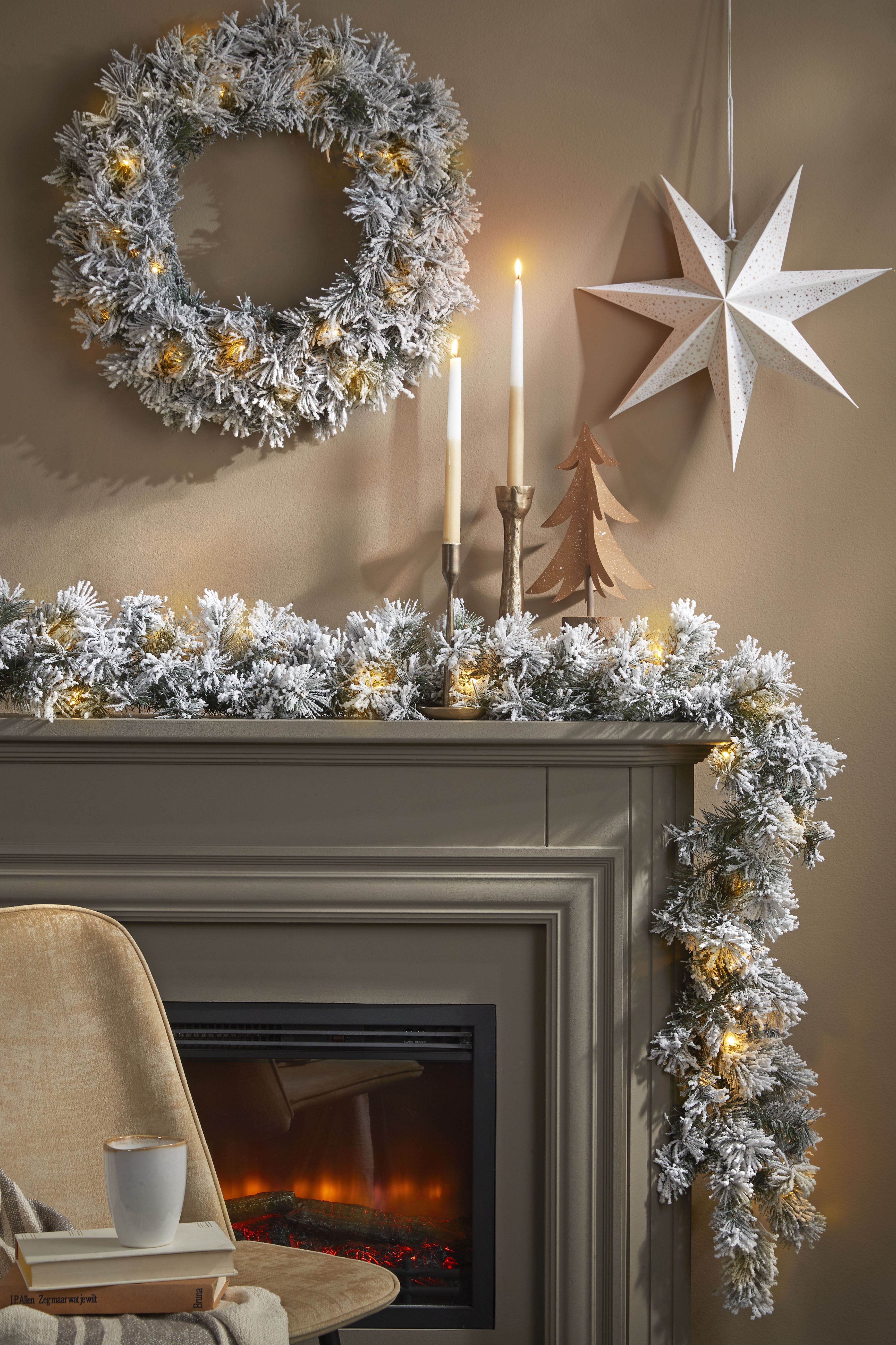 Scène festive avec couronne, guirlande, bougies et décoration en étoile. Une chaise avec un livre et une tasse.