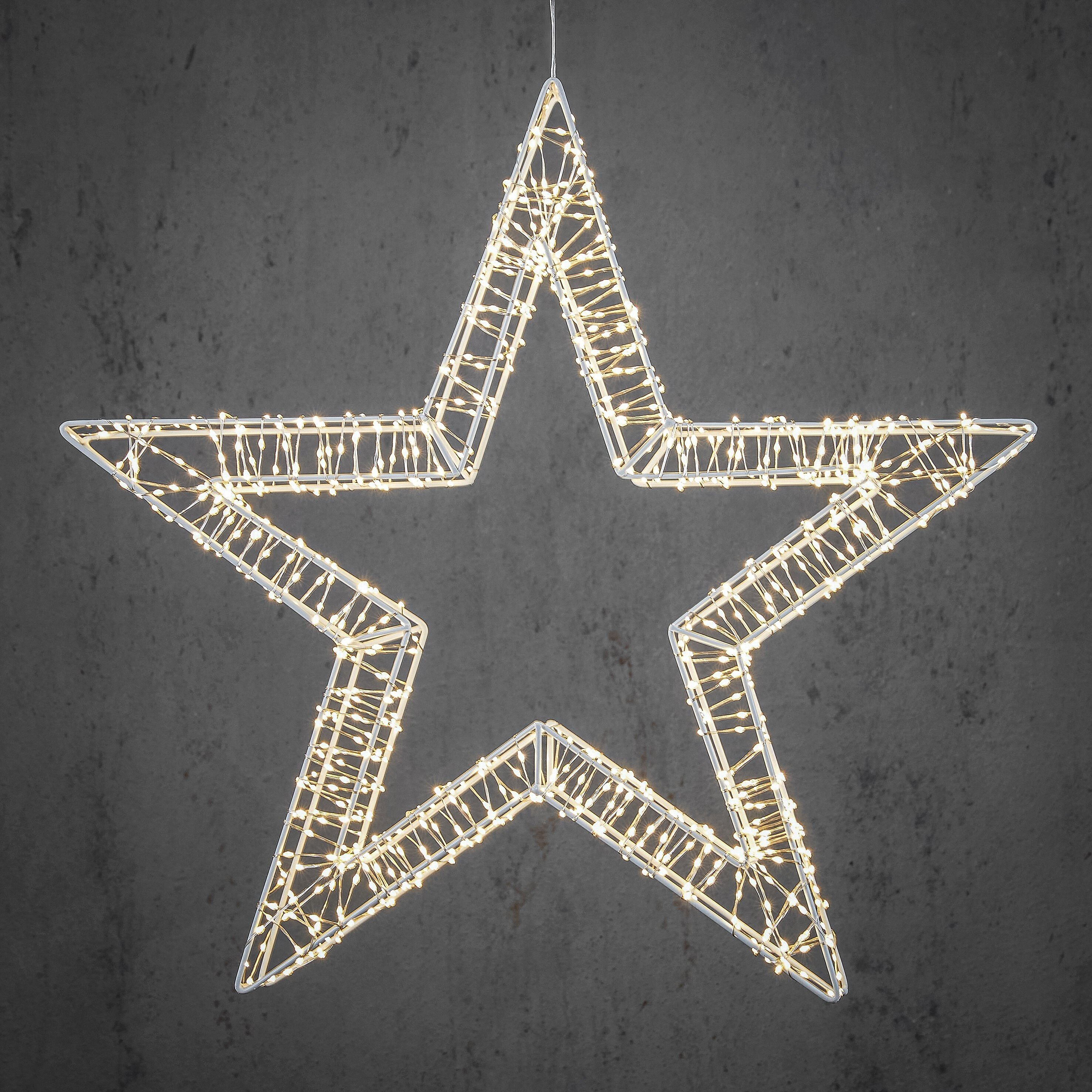 Décoration de Noël en forme d'étoile avec cadre blanc et petites lumières, sur fond gris foncé.