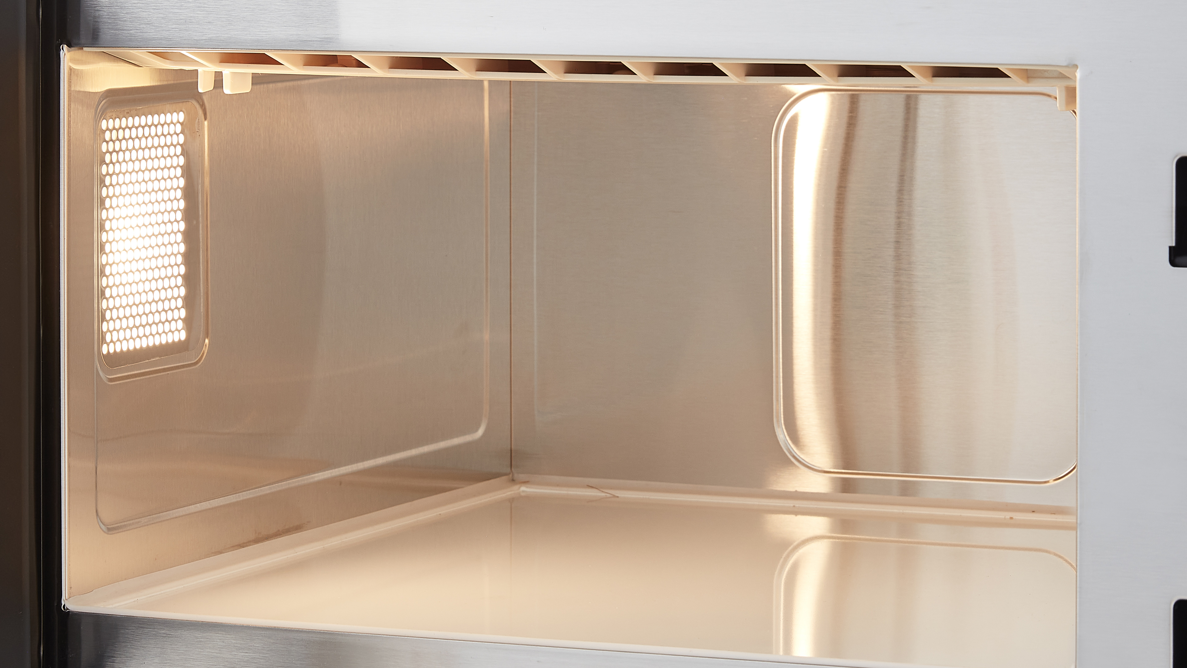 Inside of a microwave oven. The interior is stainless steel, with a light on the left and a vent at the top.