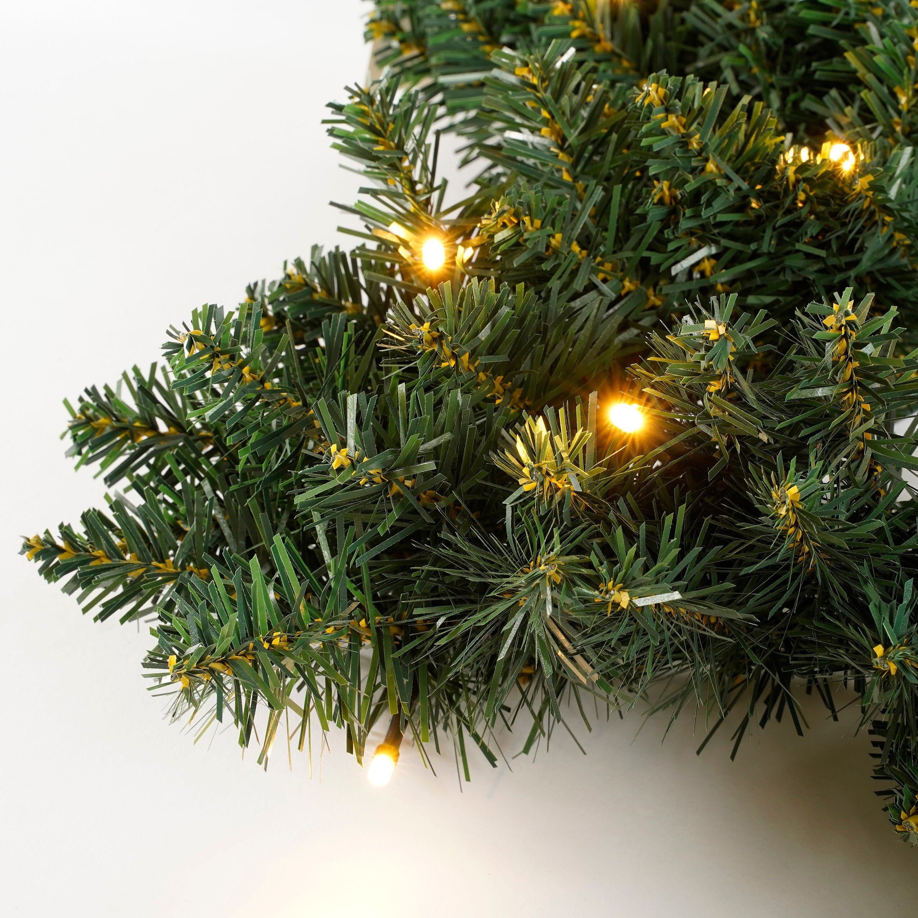 Gros plan d'une guirlande de Noël verte avec des lumières blanc chaud sur fond blanc.