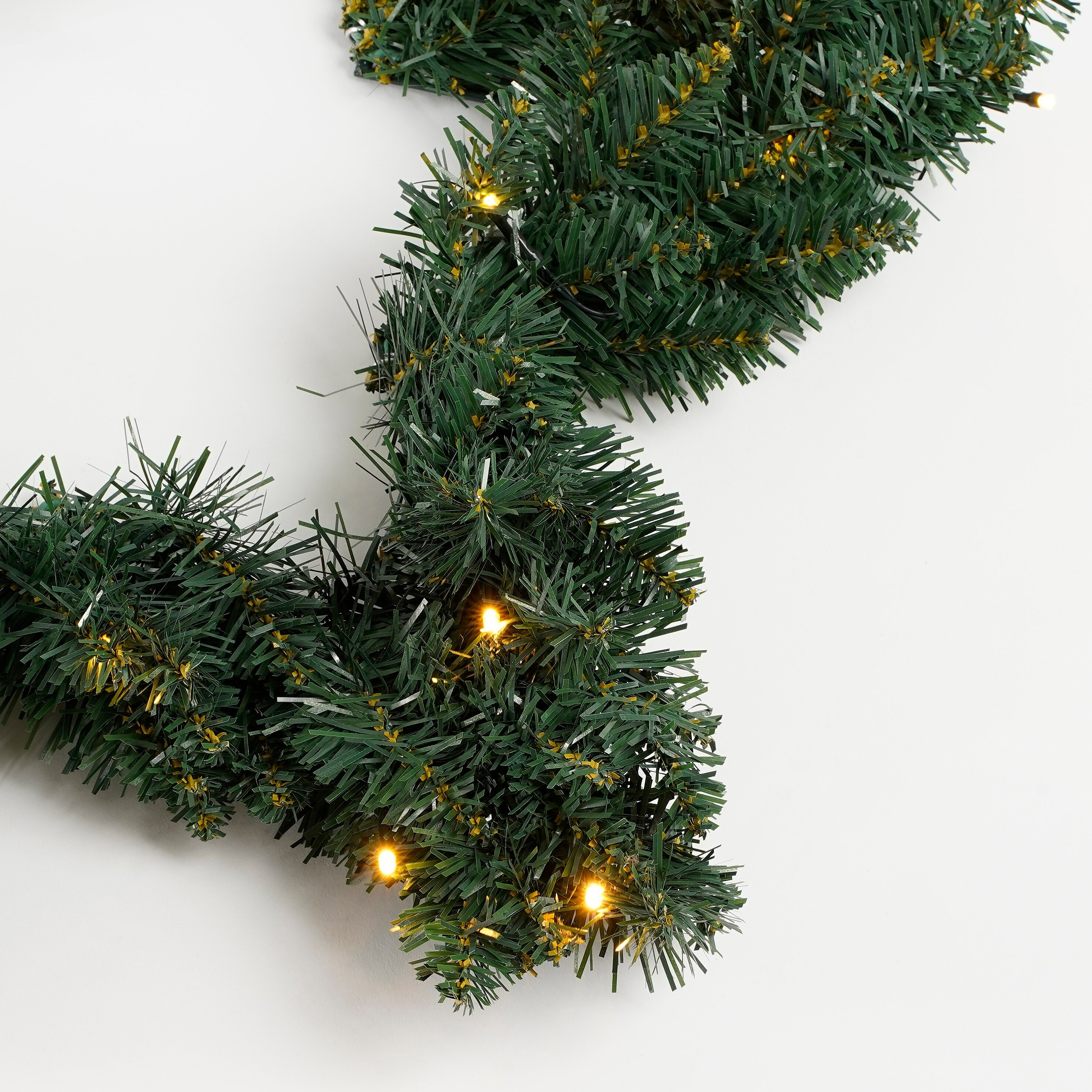 Une guirlande de Noël verte avec de petites lumières jaunes, sur fond blanc. La guirlande est incurvée.