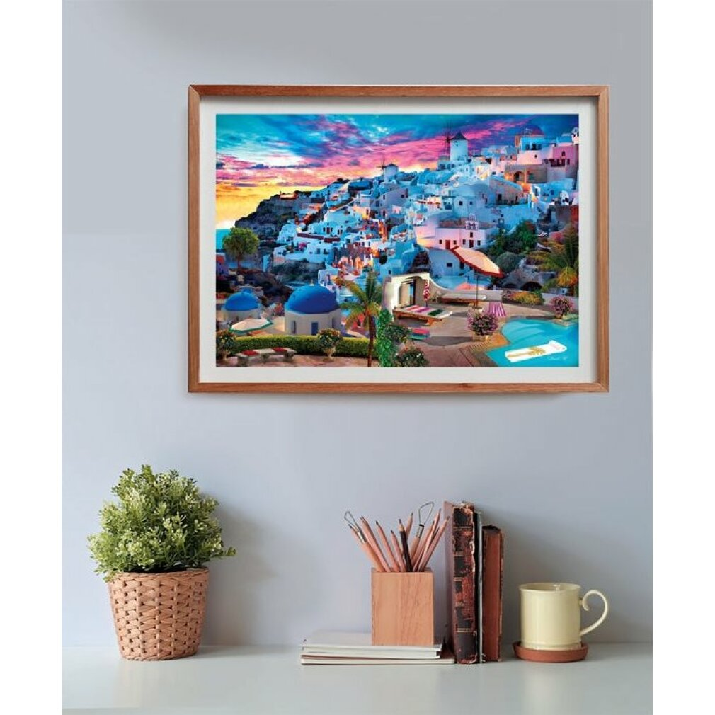 Immagine incorniciata di Santorini con edifici bianchi, cupole blu e un tramonto colorato. In primo piano una pianta, matite, libri e una tazza.