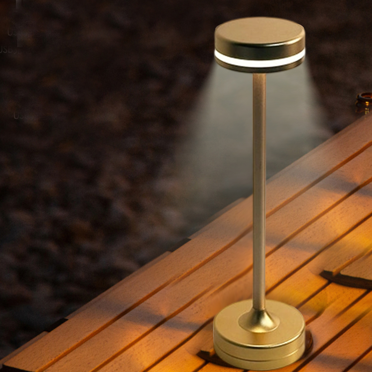Eine goldene Lampe auf einer Holzoberfläche. Die Lampe hat einen runden Fuß, einen Stiel und eine Oberseite mit Licht. Der Hintergrund ist verschwommen.