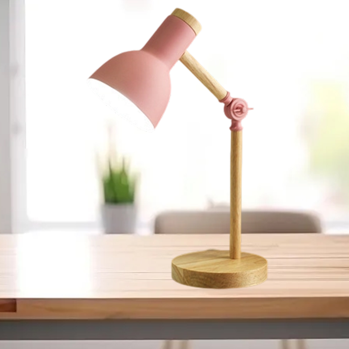 Eine rosa Schreibtischlampe mit Holzakzenten steht auf einem Holztisch. Im Hintergrund steht eine kleine Pflanze.