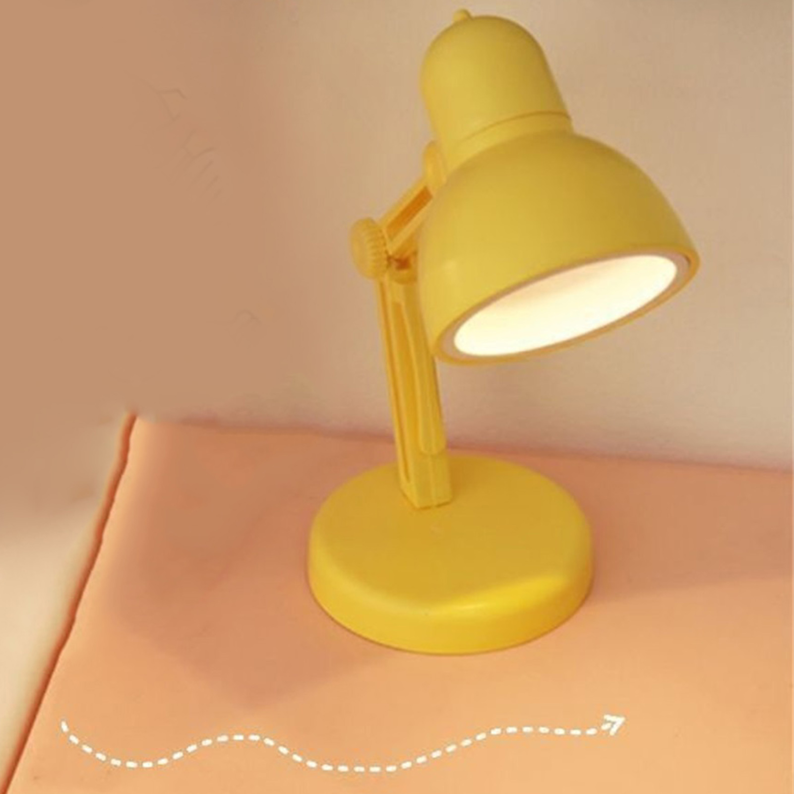 Eine gelbe Schreibtischlampe steht auf einem orangefarbenen Tisch. Die Lampe leuchtet. Der Hintergrund ist eine hellfarbige Wand.