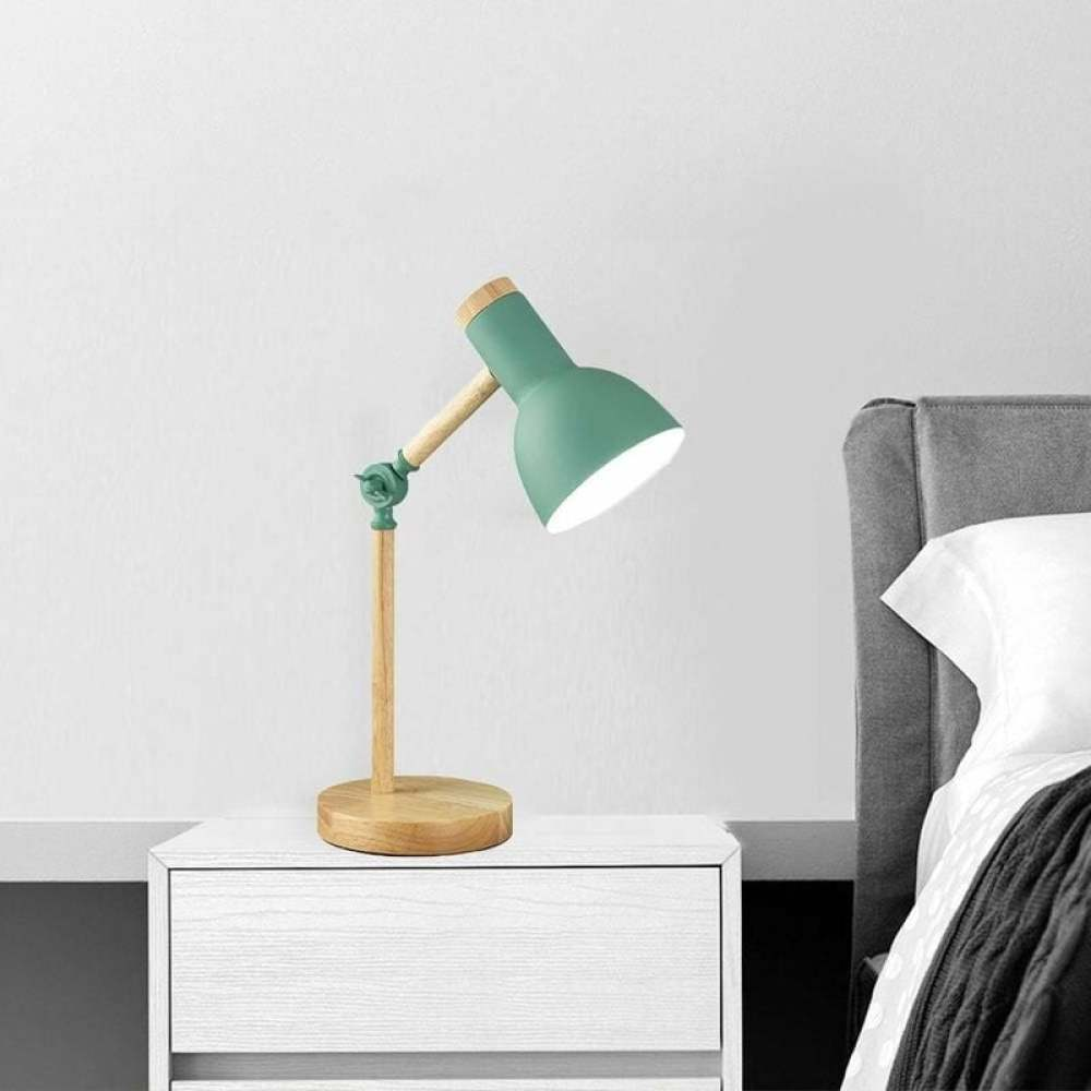 Eine grüne Schreibtischlampe mit Holzakzenten steht auf einem weißen Nachttisch. Im Hintergrund ist ein Bett mit grauem Kopfteil.