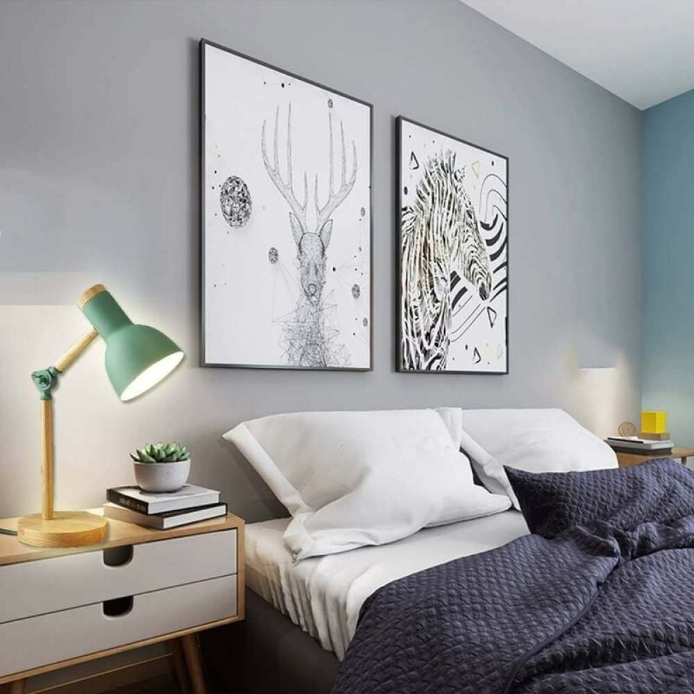 Schlafzimmer mit gerahmter Kunst, einem Bett mit weißer Bettwäsche und einer blauen Decke, einer grünen Lampe und einem Nachttisch.