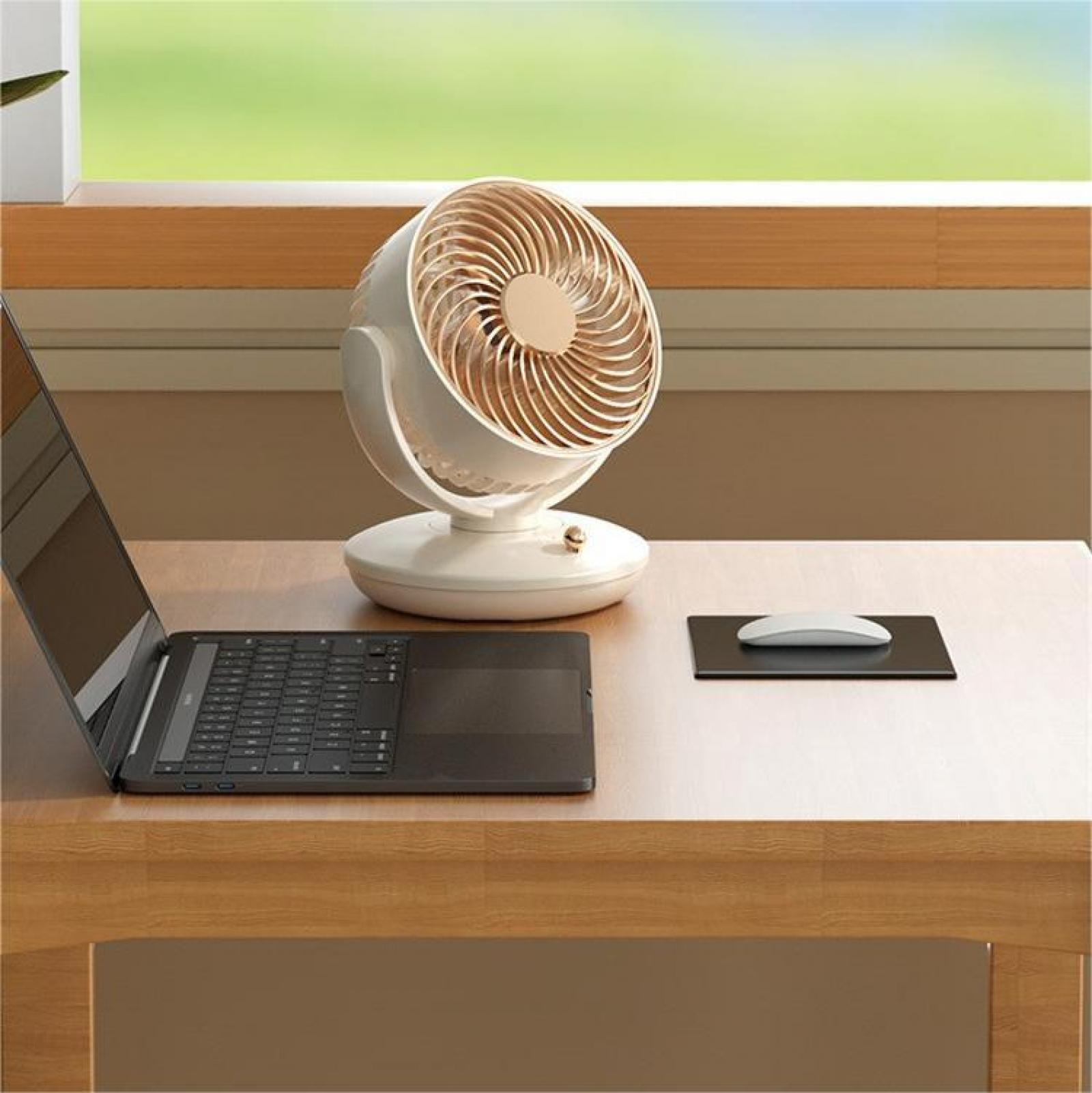 Ein Schreibtisch mit Laptop, weißem Ventilator, Maus und Mauspad. Der Hintergrund zeigt ein Fenster mit grüner Aussicht.