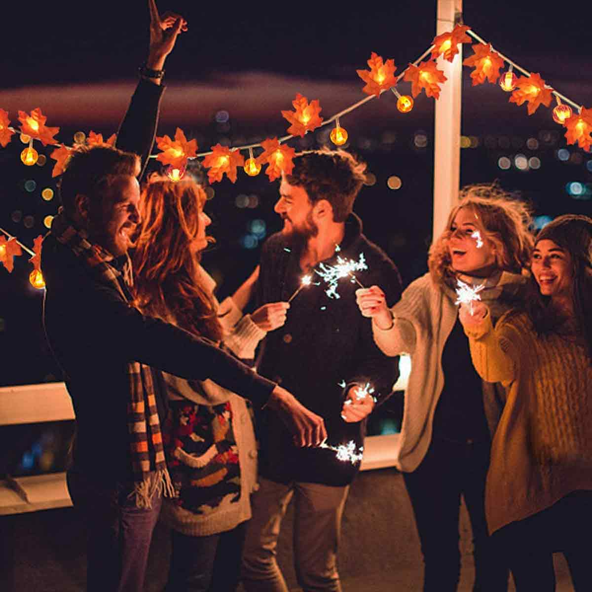 Gruppe von Menschen feiert nachts mit Wunderkerzen, beleuchtet von Lichterketten.