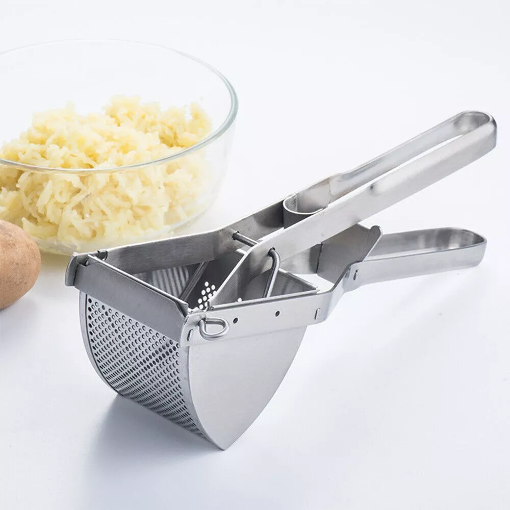 Kartoffelpresse neben einer Schüssel Kartoffelpüree und einer Kartoffel auf weißer Oberfläche.
