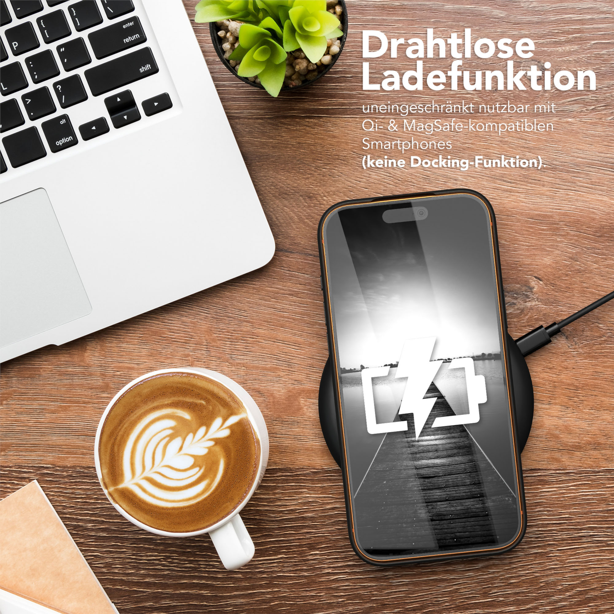 Ein Telefon, das auf einem Pad geladen wird, eine Kaffeetasse und ein Laptop stehen auf einem Holztisch, im Hintergrund eine Pflanze.