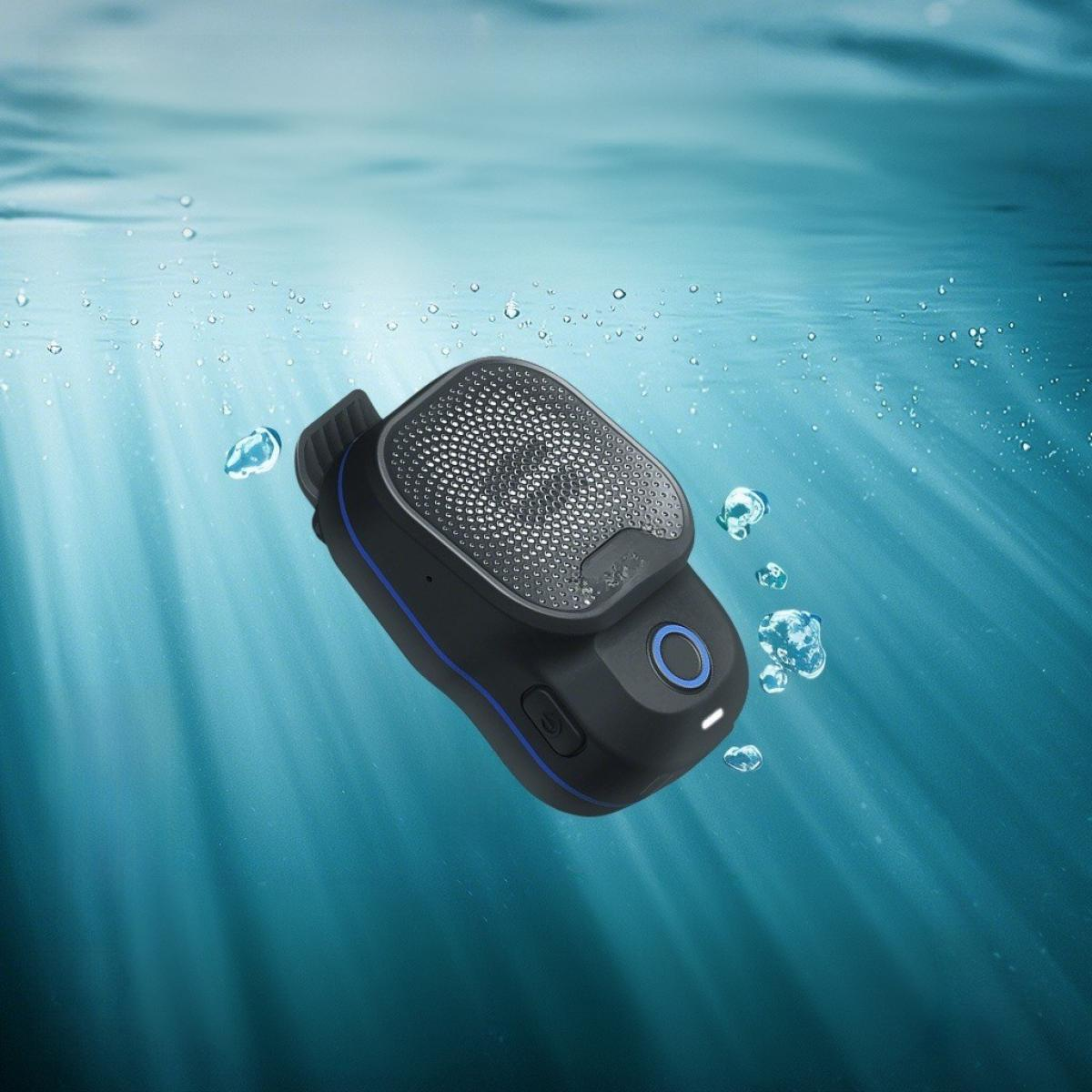 Ein schwarzes Gerät mit Lautsprecher ist in blauem Wasser mit Blasen untergetaucht. Das Gerät hat einen blauen Ring und Knopf.