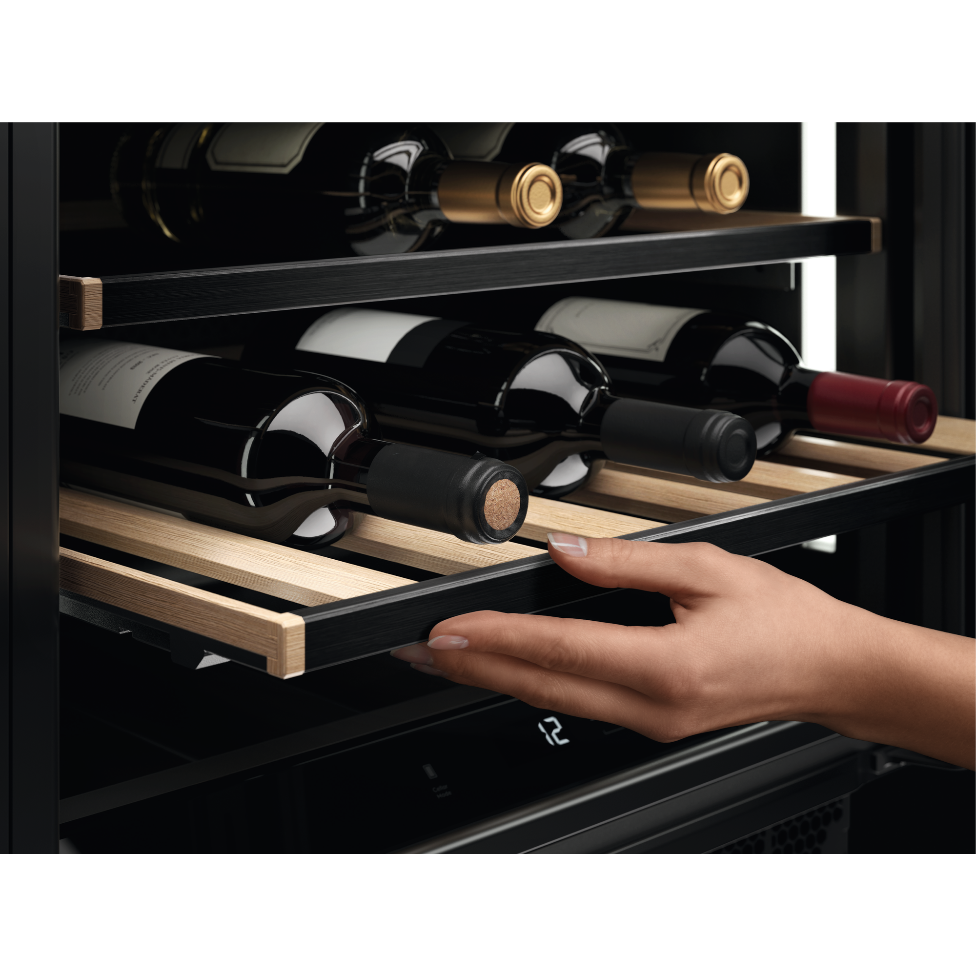 Una mano abre un cajón de nevera de vinos con varias botellas en estantes. Gabinete oscuro con estantes de madera.