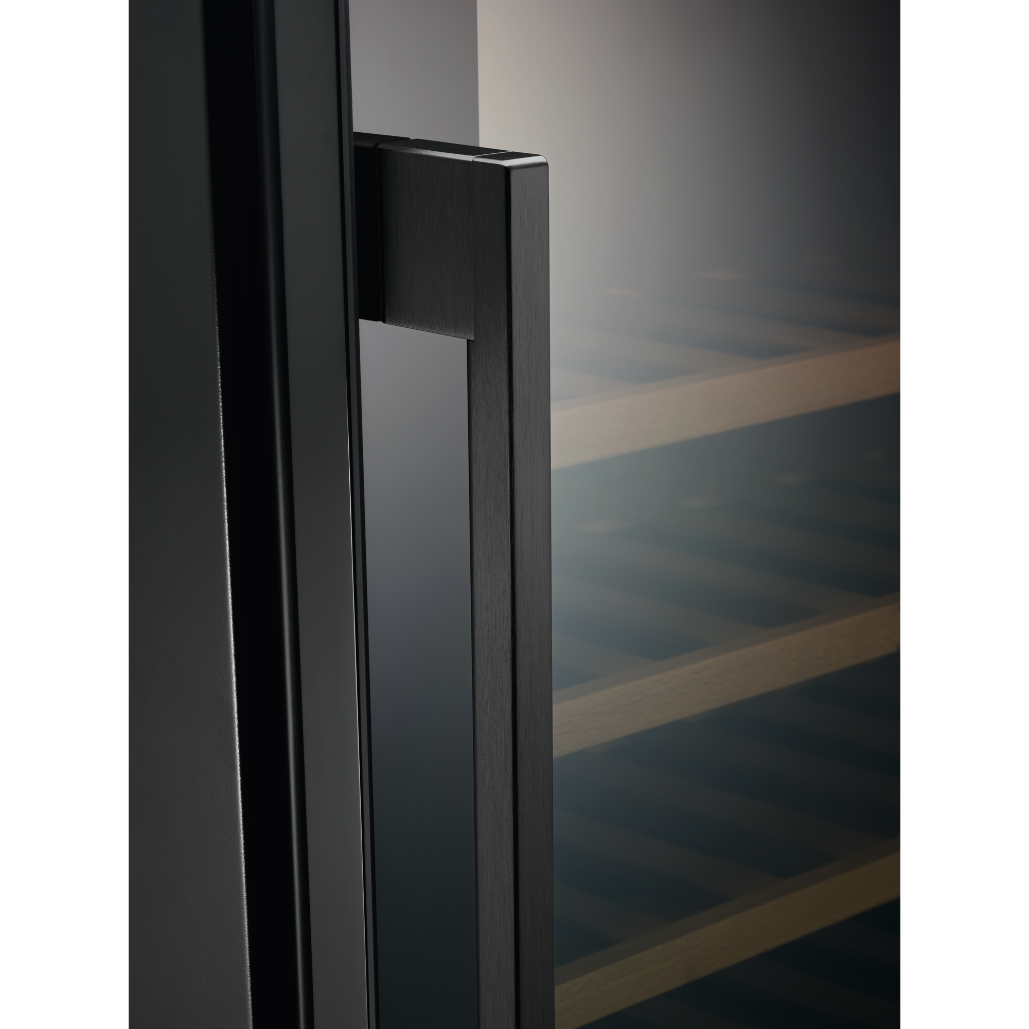 Primer plano del tirador negro de una puerta de vinoteca. Estantes de madera visibles a través del cristal. Fondo oscuro.