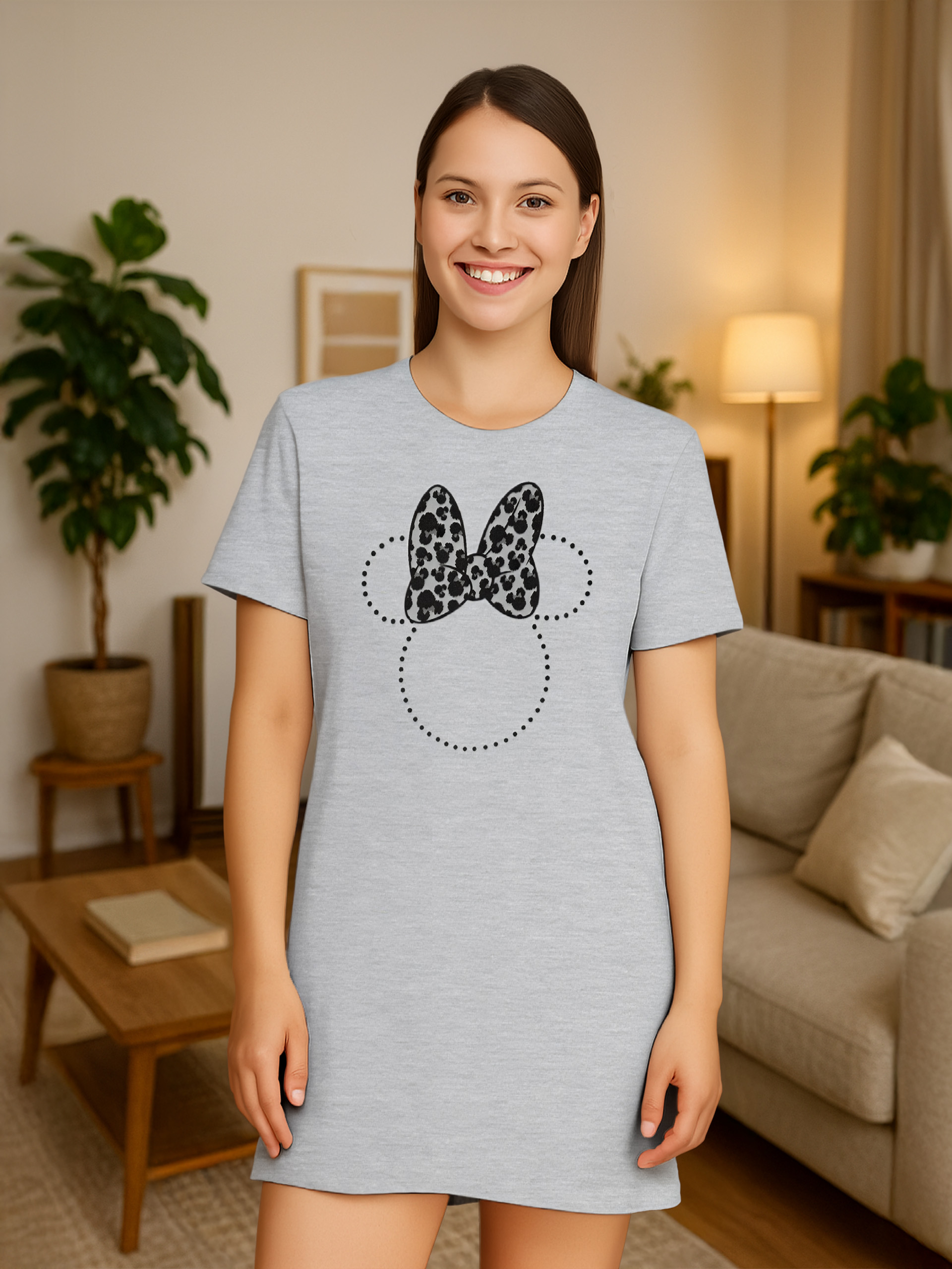 Frau in grauem Minnie-Maus-Kleid lächelt. Inneneinstellung: Pflanzen, Couch, Lampe und Tisch.