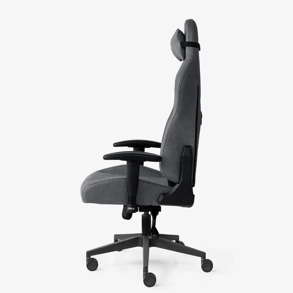 Siyah kolçaklara, tabana ve tekerleklere sahip gri ergonomik bir oyun koltuğu, beyaz bir arka plan üzerinde profilden gösteriliyor.