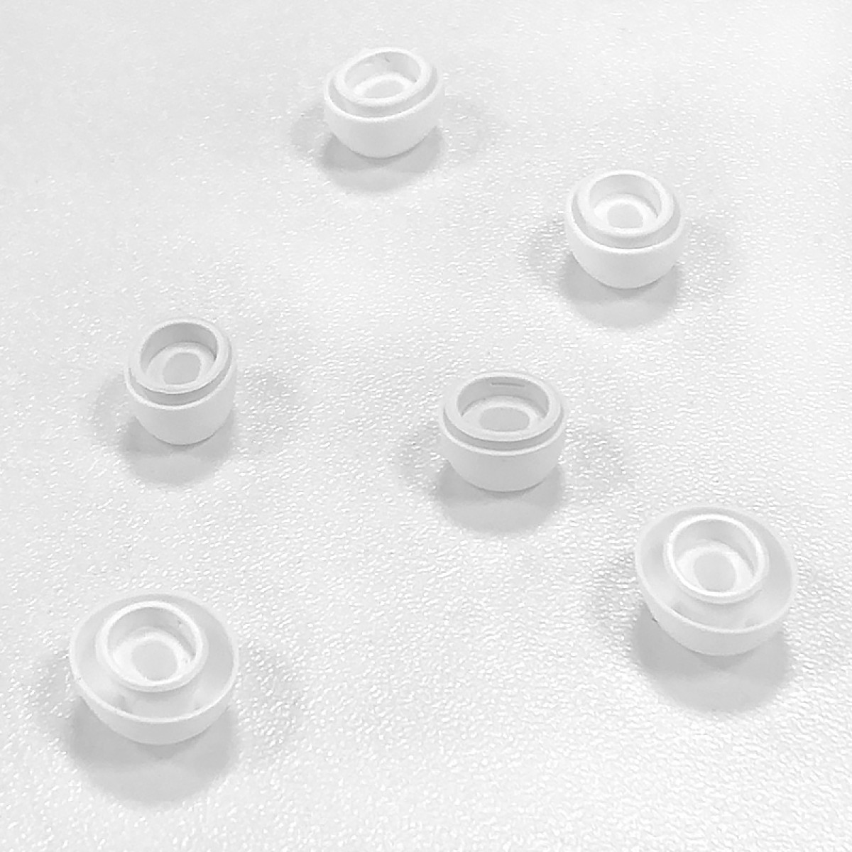 Kilka białych przedmiotów w kształcie kubków jest rozrzuconych na teksturowanej białej powierzchni. Każdy przedmiot ma centralne wgłębienie.