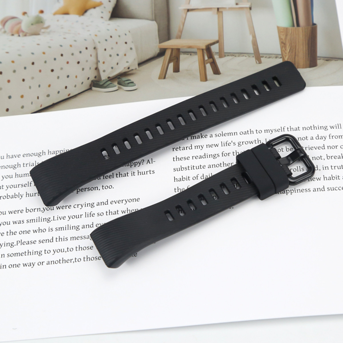 Zwei schwarze Uhrenarmbänder auf weißem Papier mit Text. Ein Bett und ein kleiner Holzstuhl sind im Hintergrund.