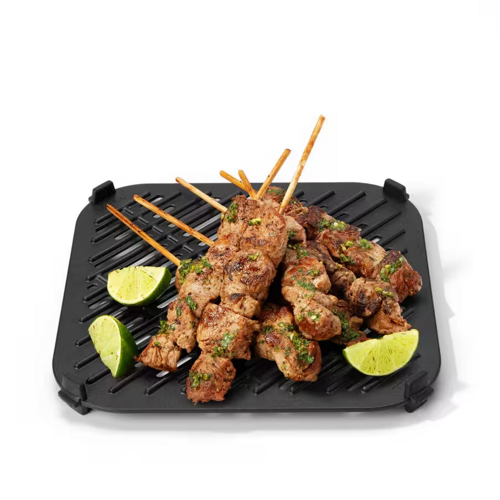 Grillowane szaszłyki mięsne na czarnej patelni grillowej z kawałkami limonki. Szaszłyki są drewniane, mięso jest brązowe, a limonka zielona.