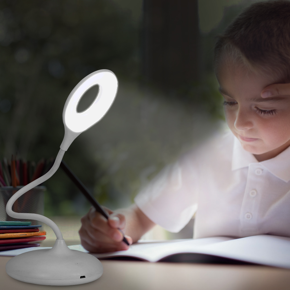 Ein Kind schreibt unter einer hellen Ringlampe an einem Schreibtisch. Ein Bleistift ist in der Hand, das Gesicht des Kindes wird vom Licht beleuchtet.