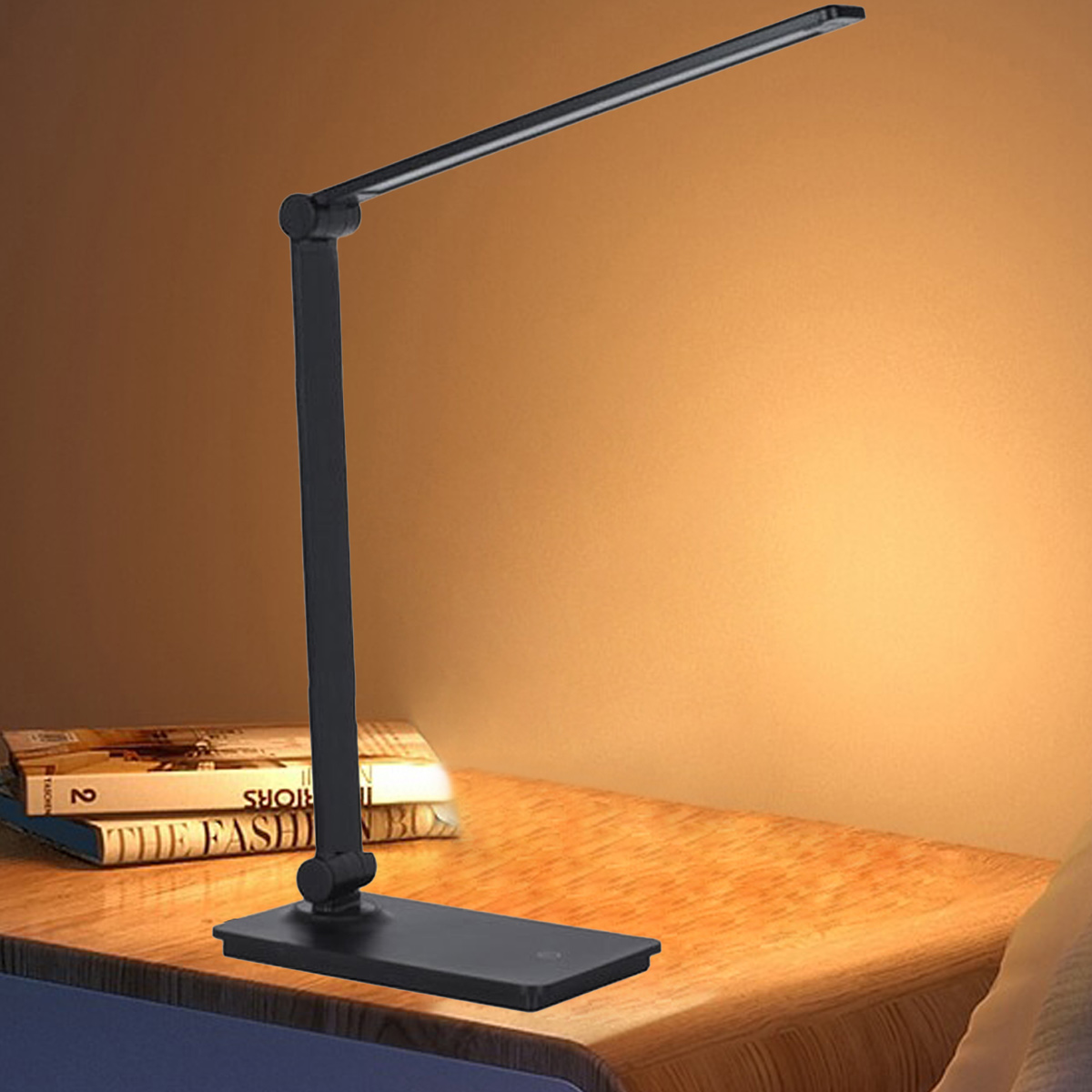 Eine schwarze Schreibtischlampe steht auf einem Holztisch mit Büchern. Der Hintergrund ist eine warm getönte Wand.