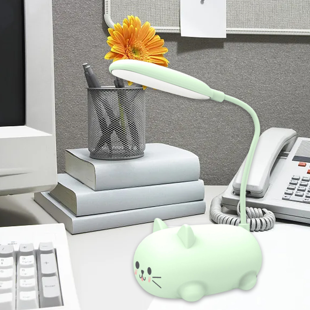 Schreibtisch mit Lampe, Blume, Büchern, Telefon und katzenförmigem Licht. Lampe und Licht sind grün. Tastatur links.