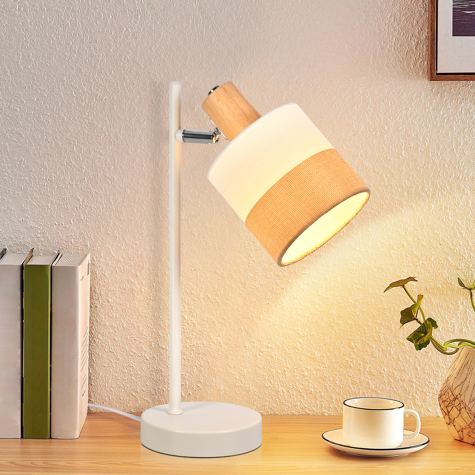 Una lampada da scrivania con base e stelo bianchi e un paralume con sezioni beige e bianche. Sono visibili anche libri e una tazza.