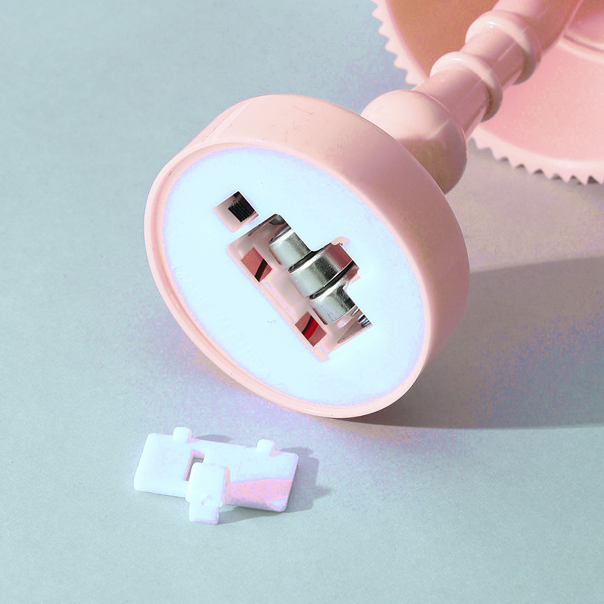 Ein rosa Küchengerät mit weißem Innenraum und silbernen Metallteilen. Zwei weiße Teile liegen auf der grauen Oberfläche.