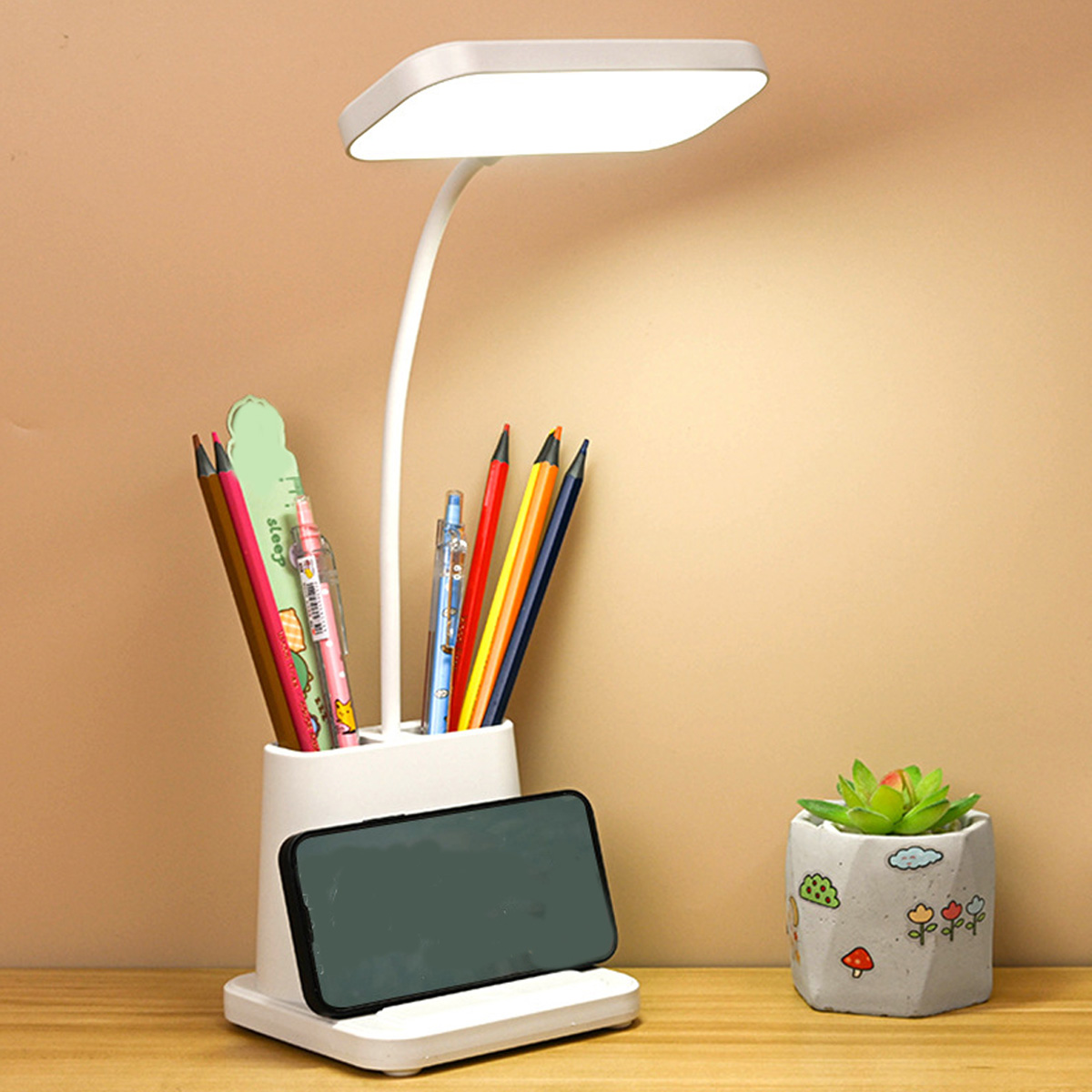 Eine Schreibtischlampe mit Stifthalter und Telefonständer. Daneben eine kleine Sukkulenten. Stifte und Stifte befinden sich im Halter.
