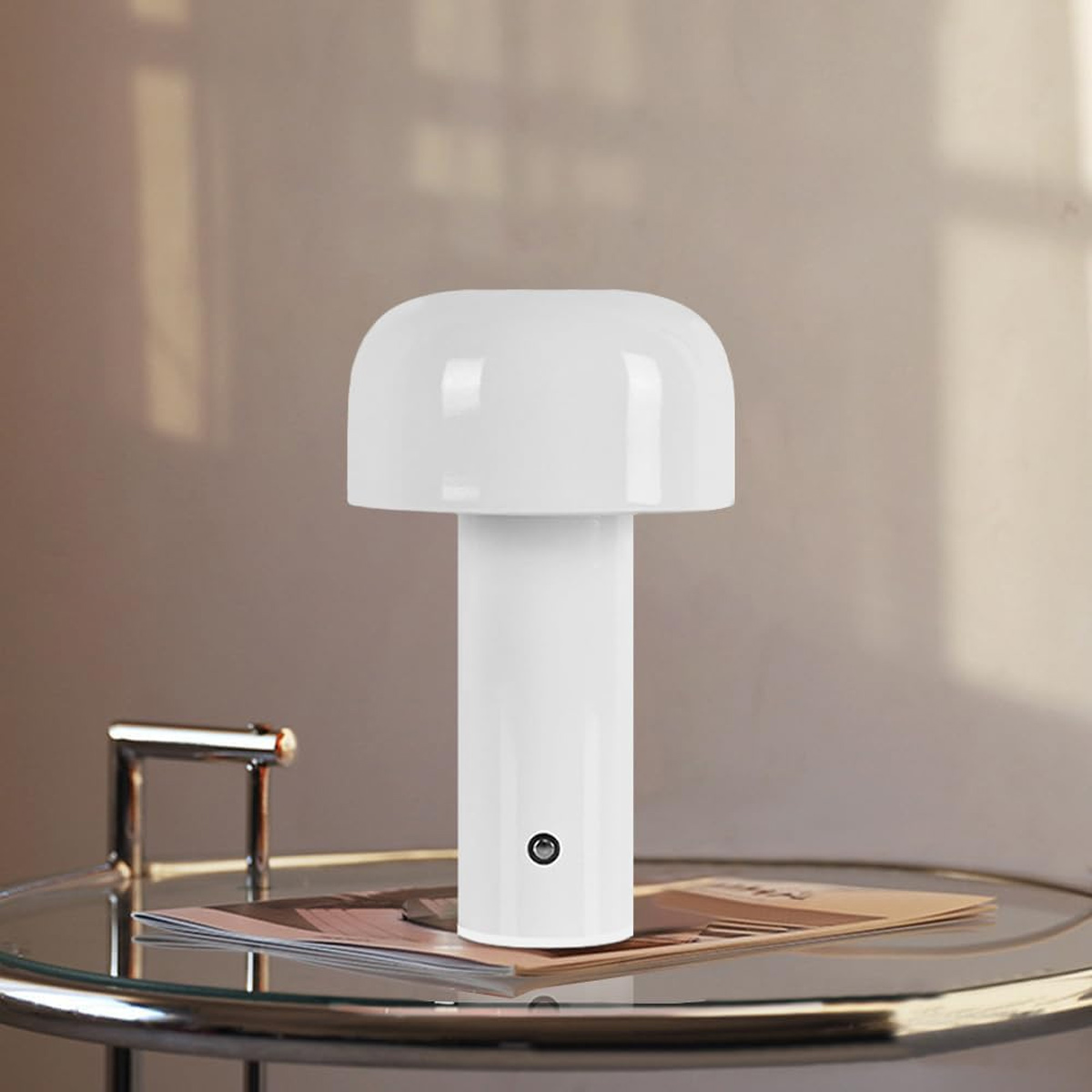 Eine weiße pilzförmige Lampe steht auf einem Glastisch. Auf dem Tisch liegen ein Magazin und ein Metallständer. Der Hintergrund ist eine beige Wand.