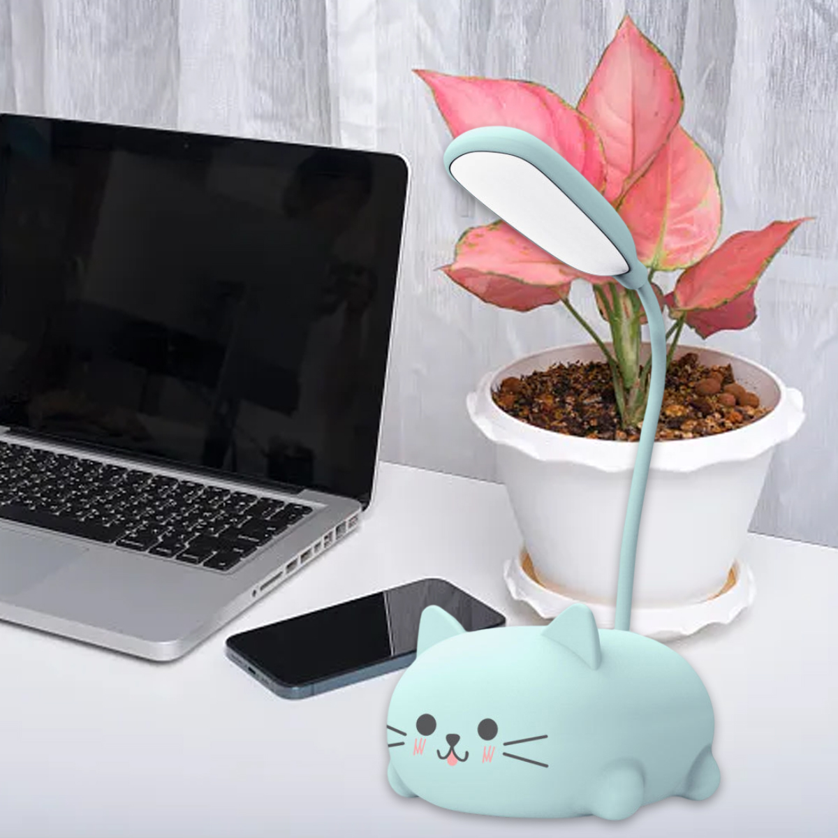Ein Schreibtisch mit Laptop, Telefon, katzenförmiger Lampe und Pflanze. Die Pflanze hat rosa Blätter. Die Lampe ist an.