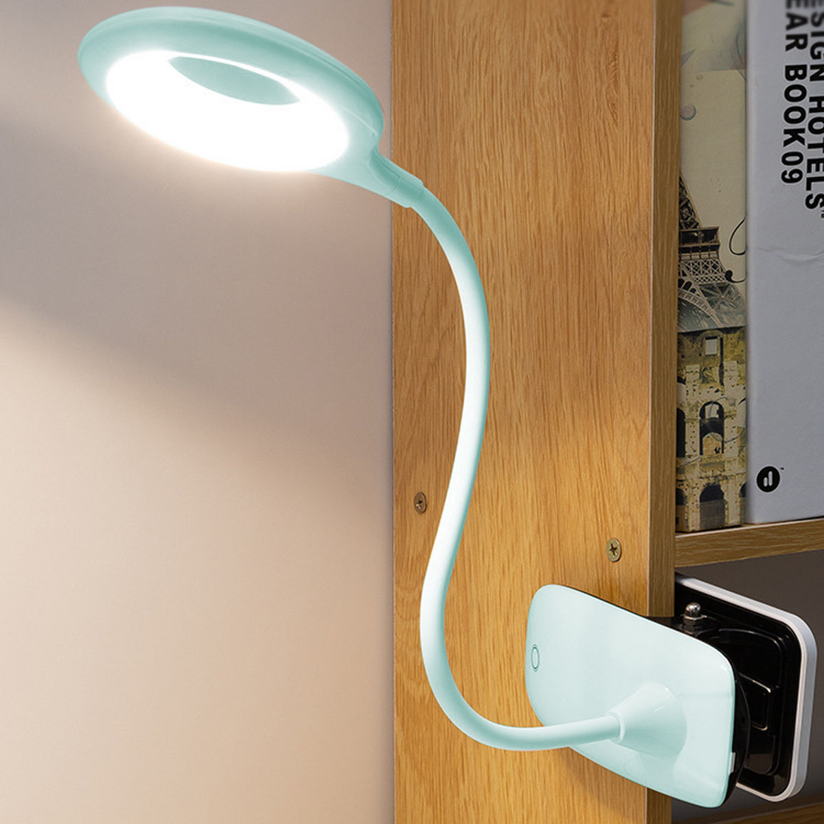 Eine mintgrüne Schreibtischlampe ist an einem Holzregal befestigt. Die Lampe ist eingeschaltet und beleuchtet den Bereich. Bücher sind im Hintergrund.