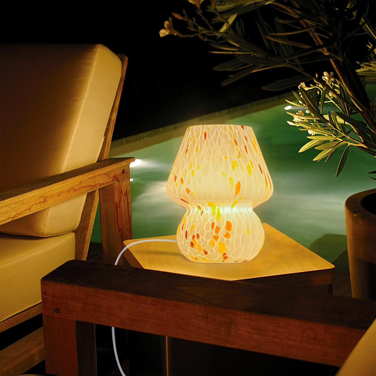 Eine pilzförmige Lampe mit bunten Flecken steht zwischen Holzstühlen. Im Hintergrund ist ein Pool zu sehen.