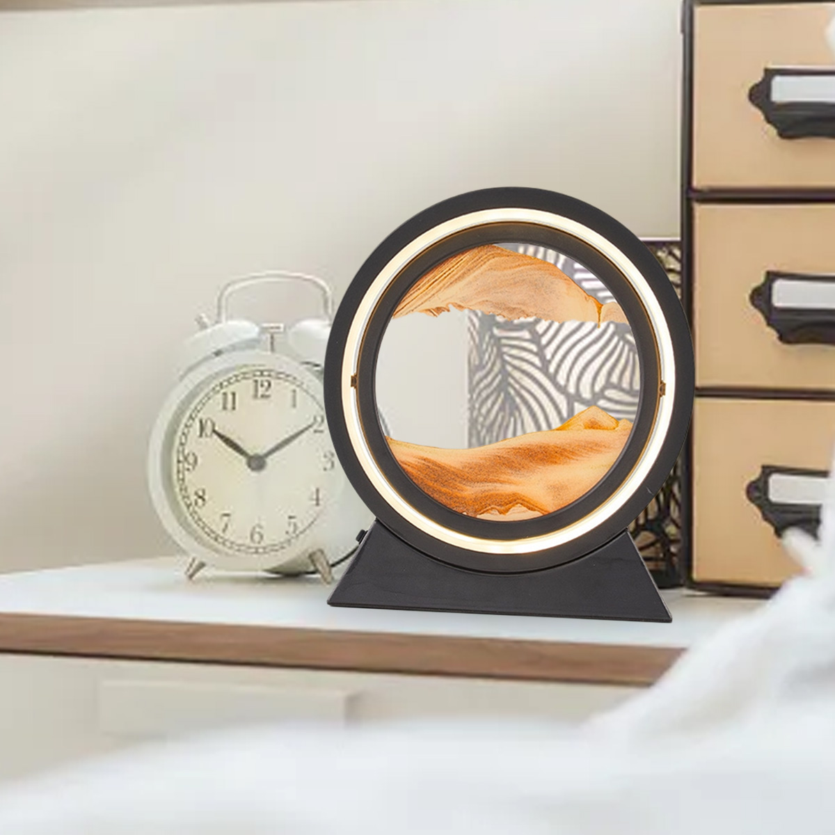 Eine runde Sandkunstlampe mit orangefarbenem Sand, einer weißen Uhr und Boxen auf einer weißen Oberfläche.
